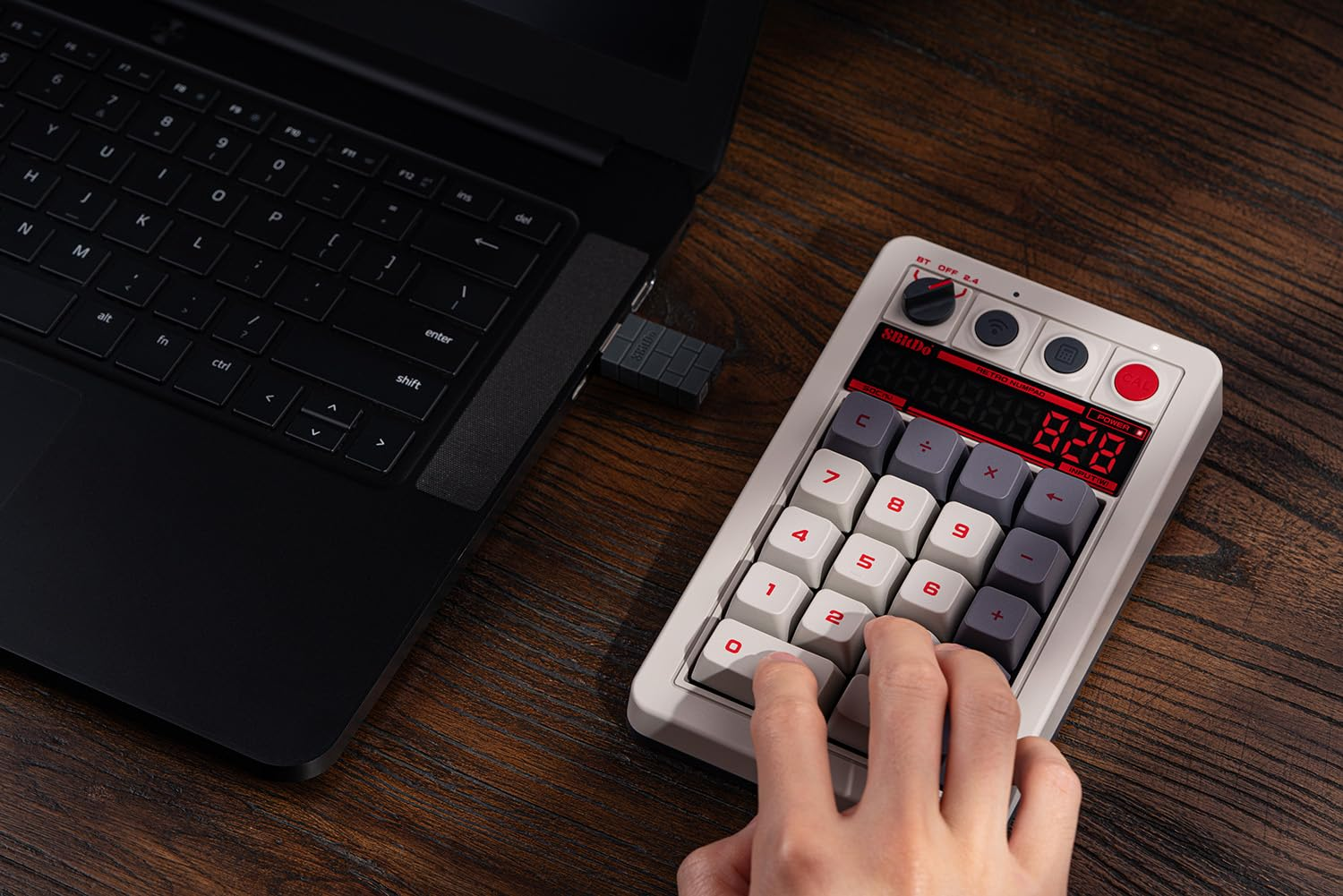 Osoba używa retro klawiatury numerycznej kalkulatora podłączonej do laptopa. Klawiatura numeryczna wyświetla liczbę.