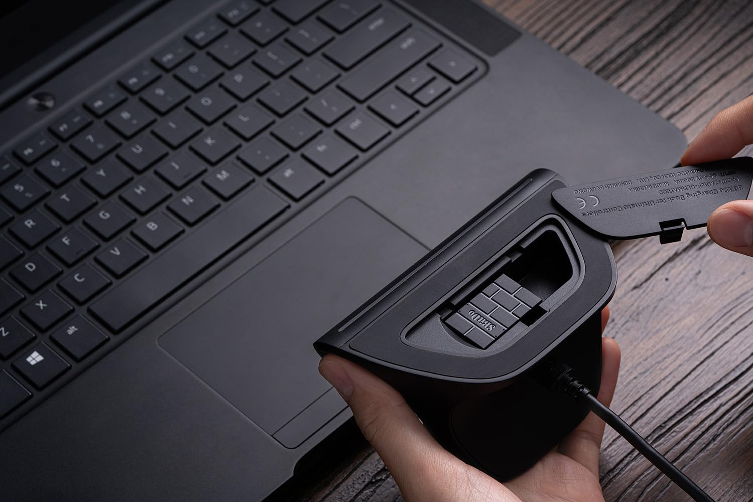 Le mani di una persona rimuovono il coperchio del vano batteria da un dispositivo collegato a un laptop.