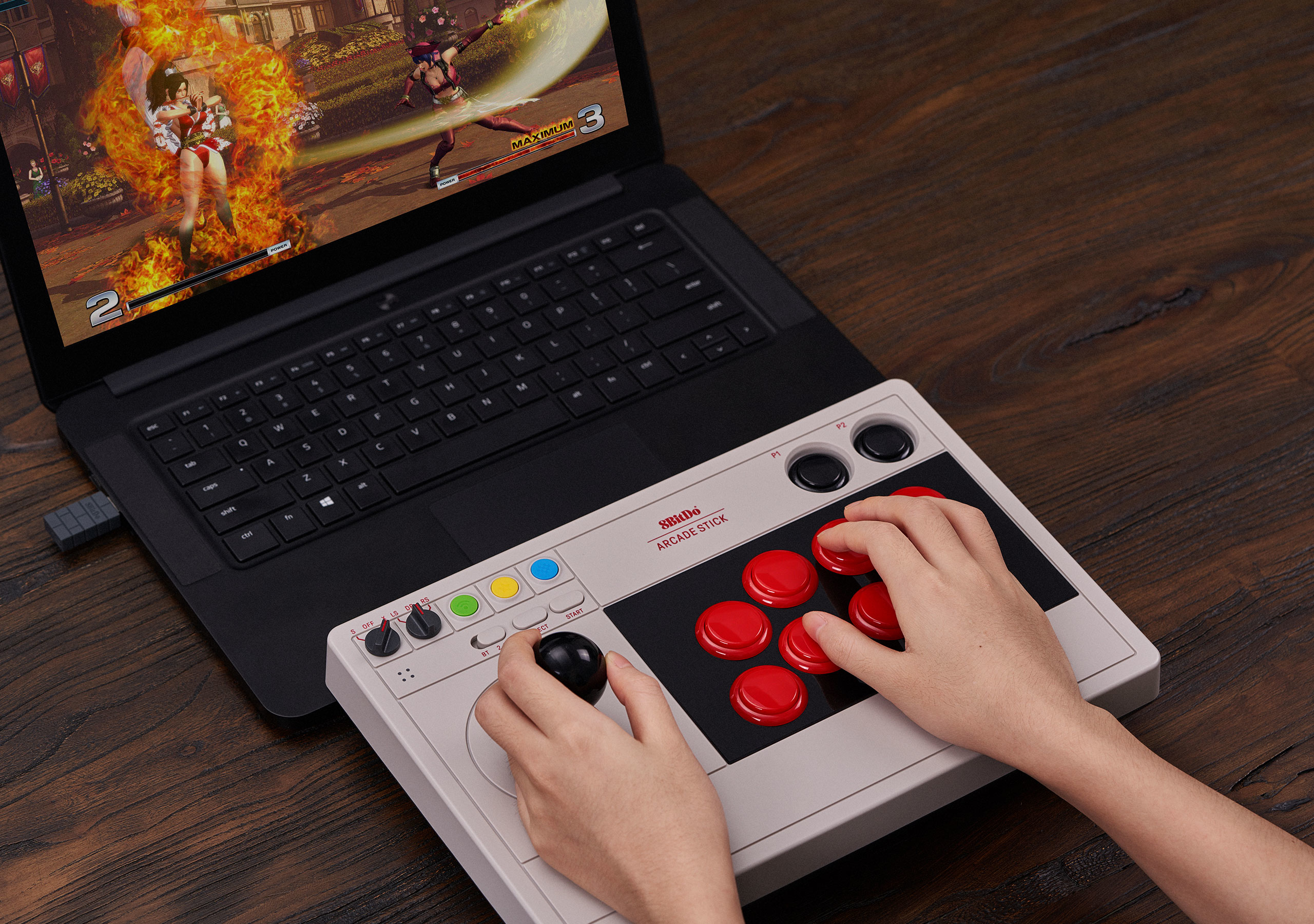 Mani che usano un arcade stick collegato a un laptop con un gioco di combattimento su legno.