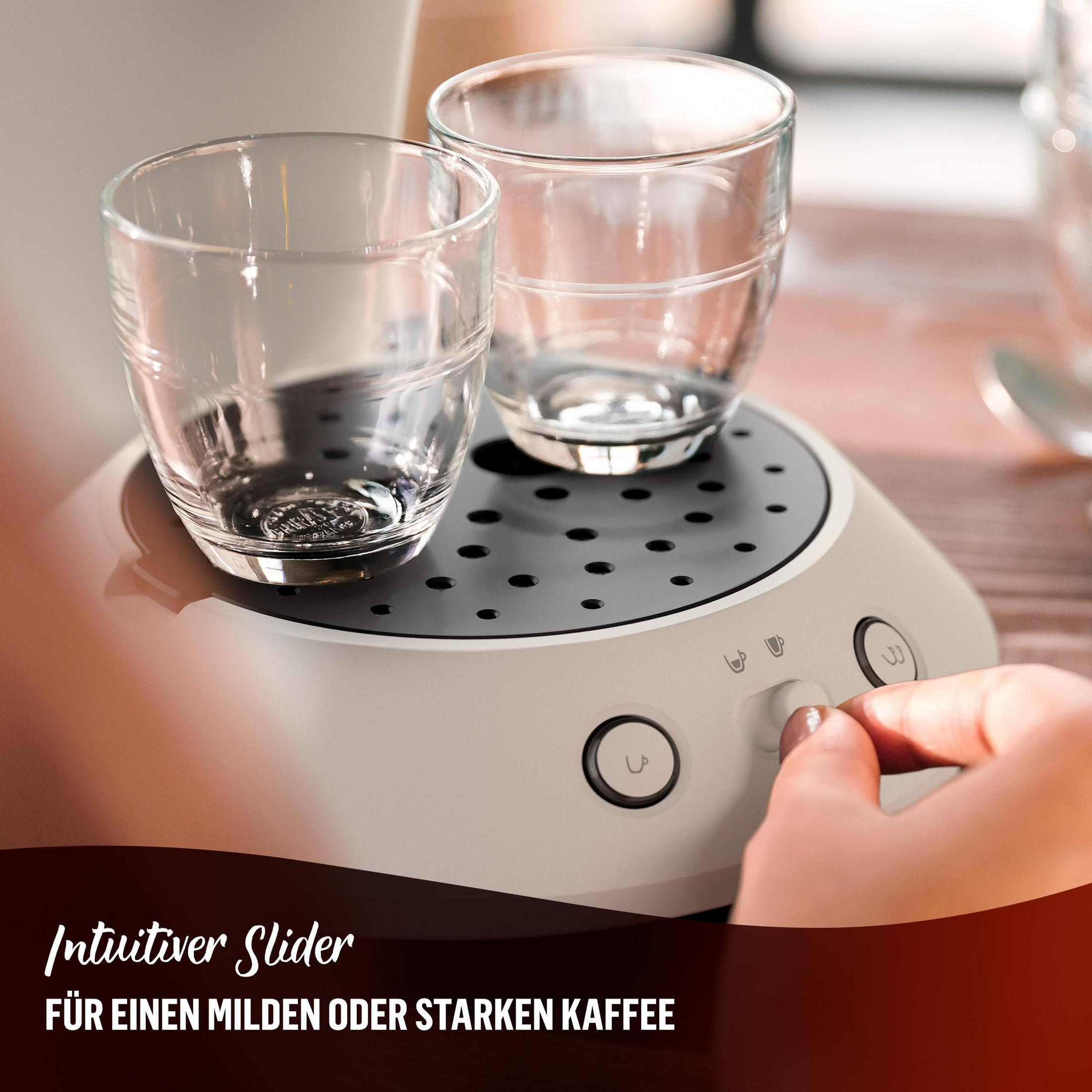 Nahaufnahme des Kaffeemaschinensockels mit zwei Gläsern. Eine Hand stellt Einstellungen ein.