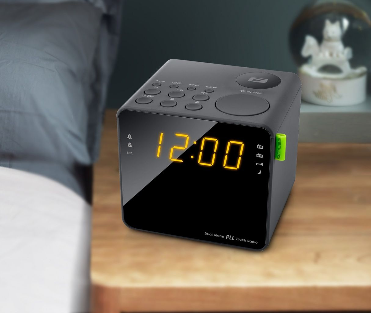 Czarny budzik na stoliku nocnym. Wyświetlana jest godzina 12:00. Widoczne przyciski i elementy sterujące.