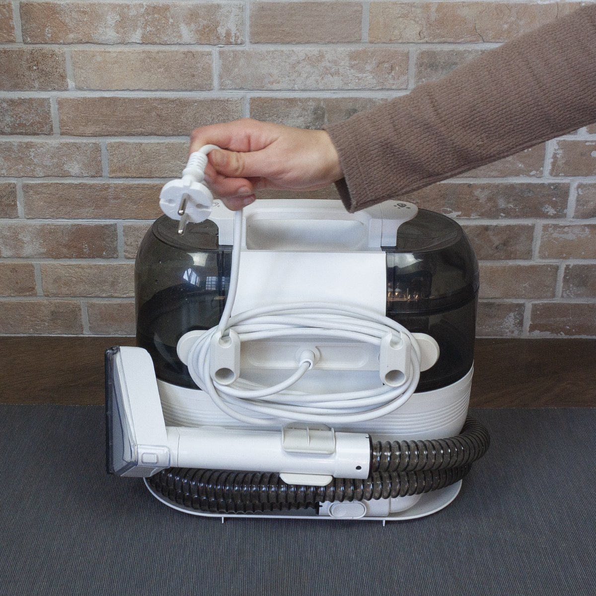 Ręka trzymająca wtyczkę i przewód odkurzacza.