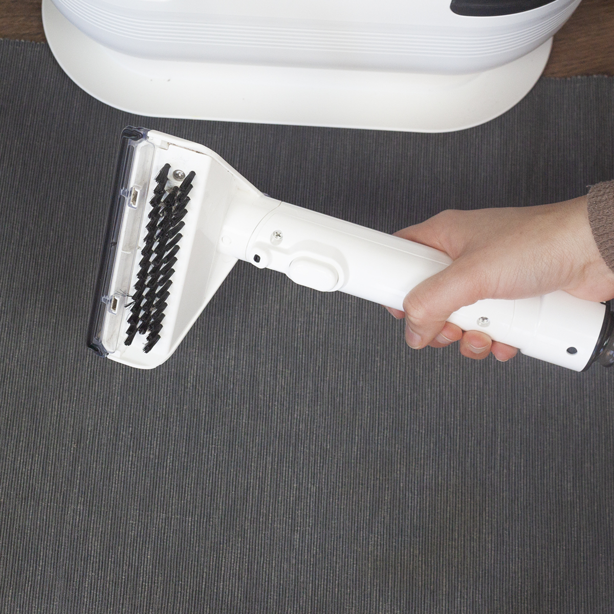 Ręka trzymająca białą przystawkę do maszyny czyszczącej nad szarą powierzchnią.