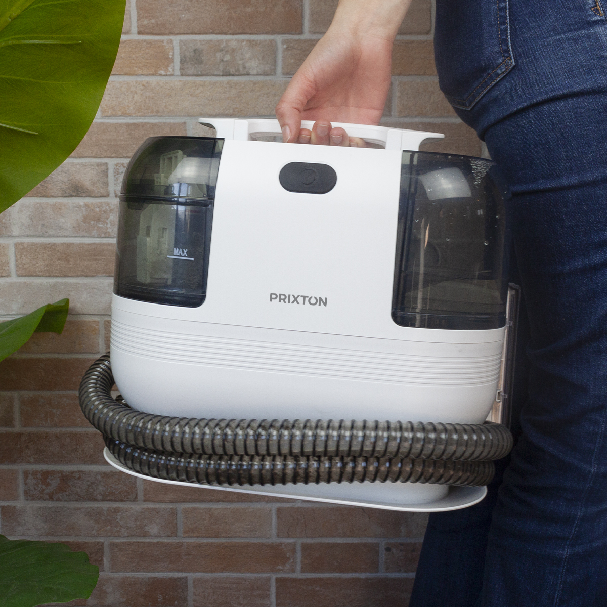 A woman carrying a vacuum cleaner with a hose, next to a brick wall.