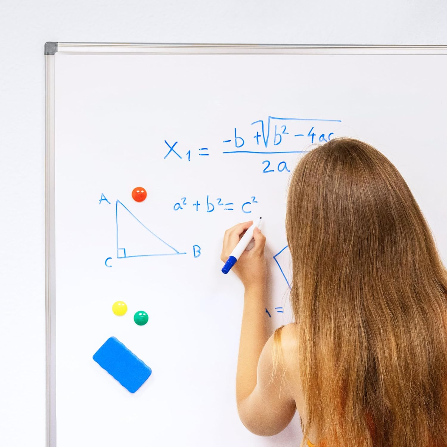 Una mujer escribe ecuaciones matemáticas en una pizarra con marcadores e imanes.
