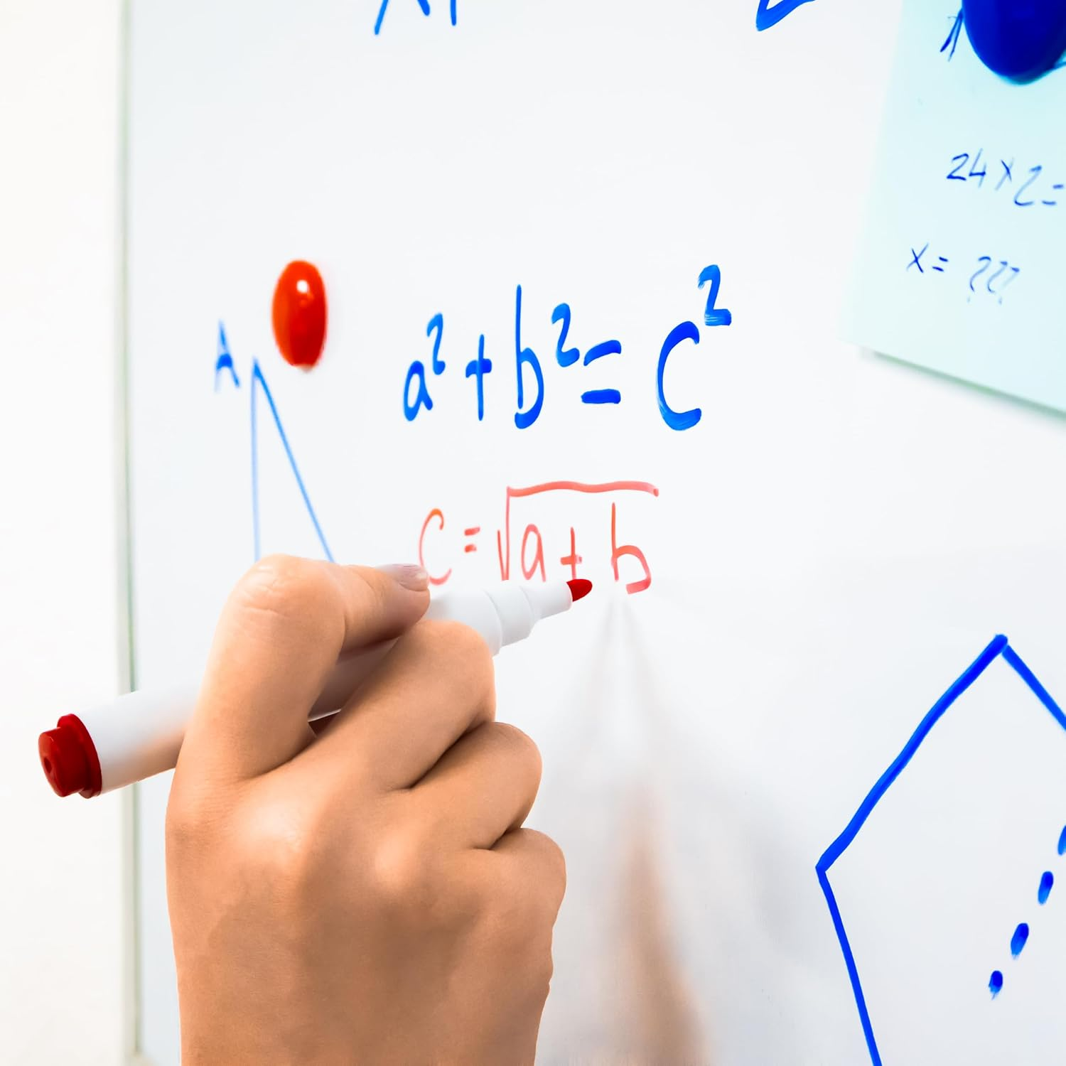 Una mano escribiendo ecuaciones matemáticas en una pizarra con un rotulador rojo. Es visible una nota adhesiva azul.