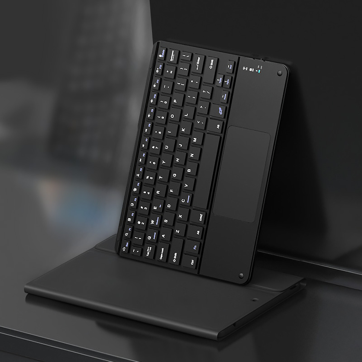 Eine schwarze kabellose Tastatur mit Touchpad, die auf einer gefalteten Abdeckung vor einem dunklen Hintergrund steht.