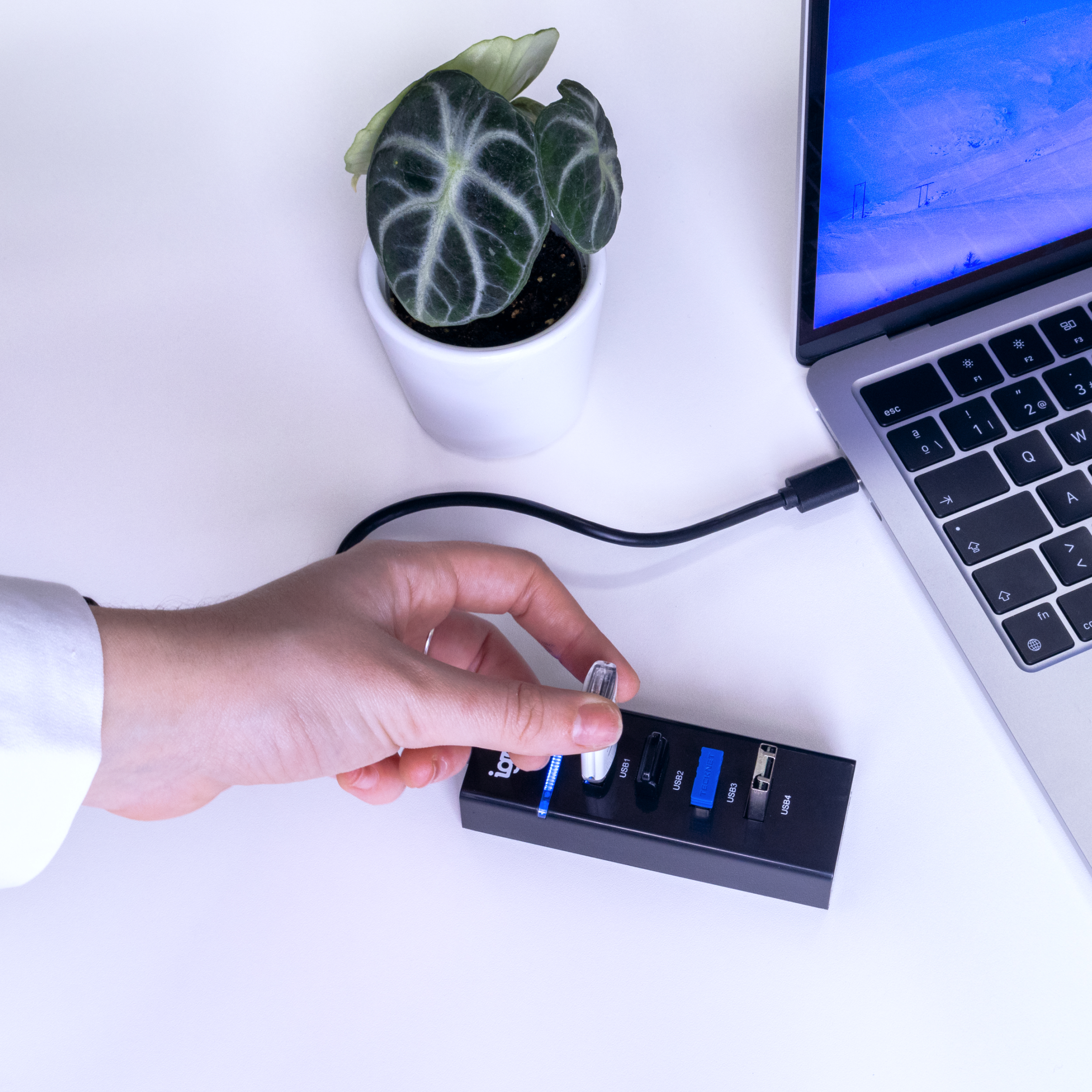 Mano insertando una memoria USB en un concentrador USB conectado a una laptop.