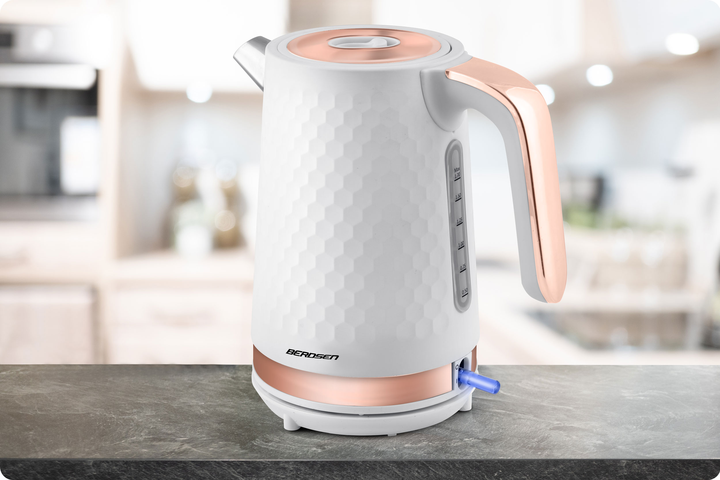 Biały i różowo-złoty czajnik elektryczny. Posiada wzór plastra miodu, rozmyte tło kuchni.