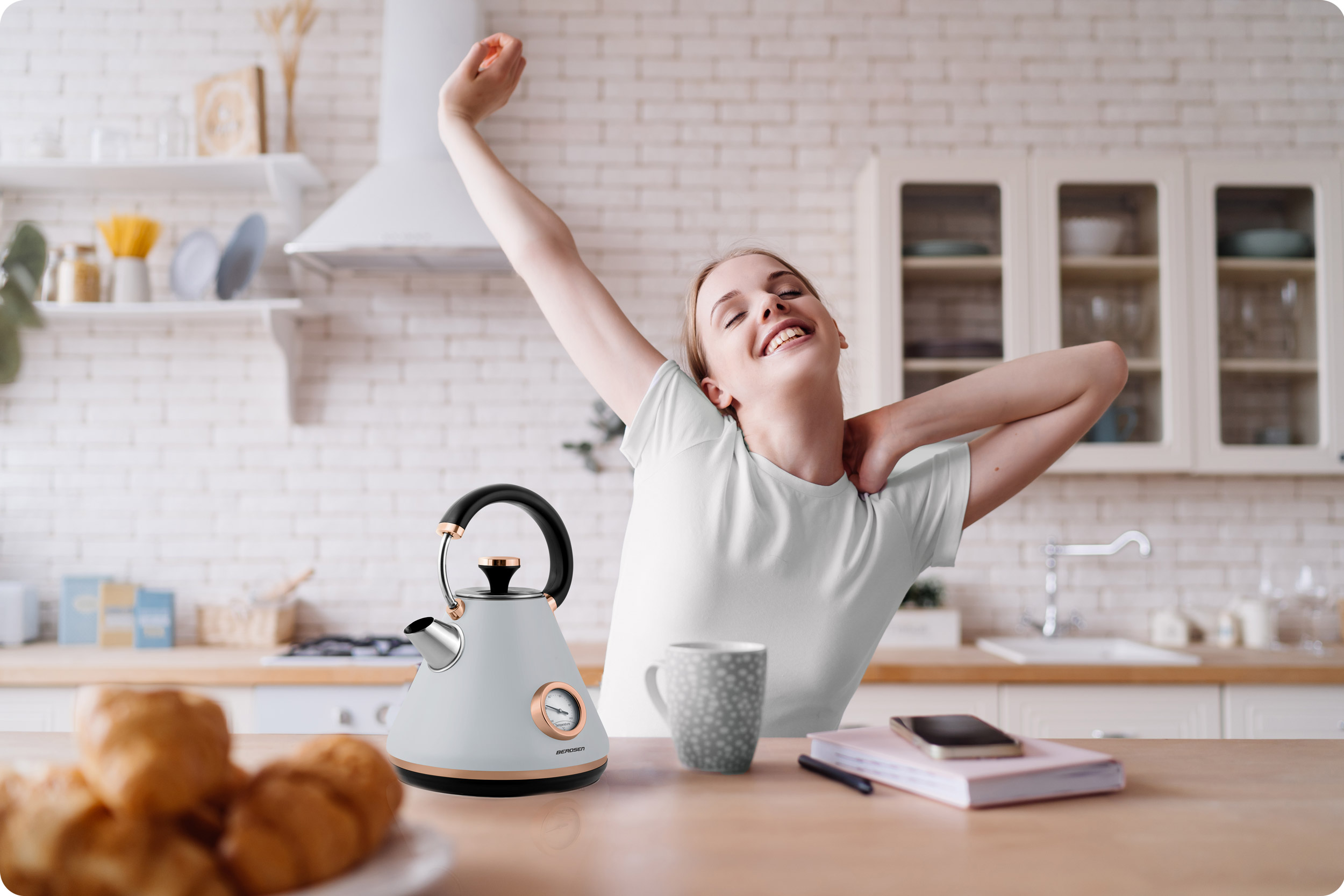 Kobieta w kuchni rozciąga się, a na stole biały czajnik i produkty śniadaniowe.