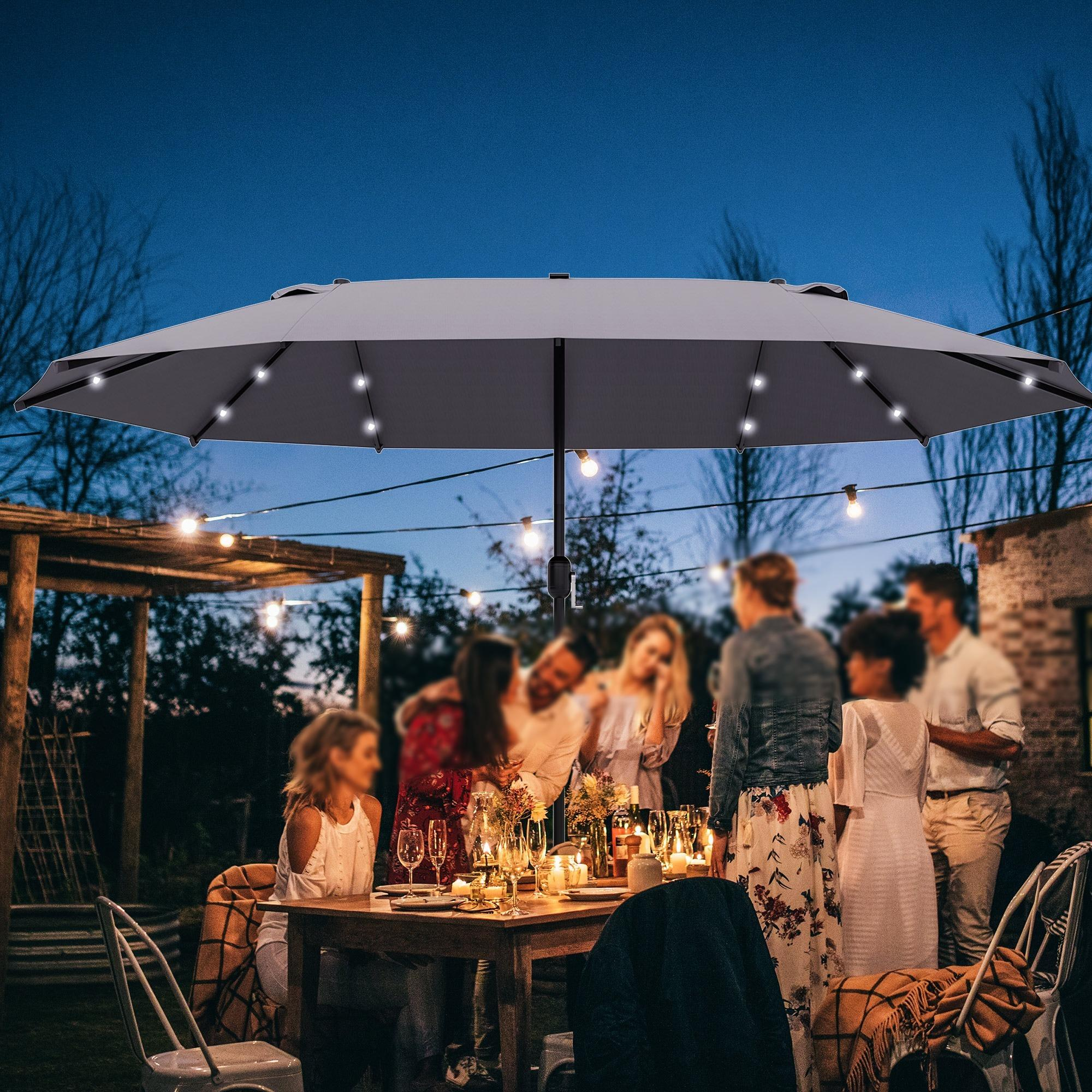 Eine Gruppe von Leuten versammelt sich an einem Tisch unter einem dunkelgrauen Sonnenschirm mit Lichtern. Abendszene.