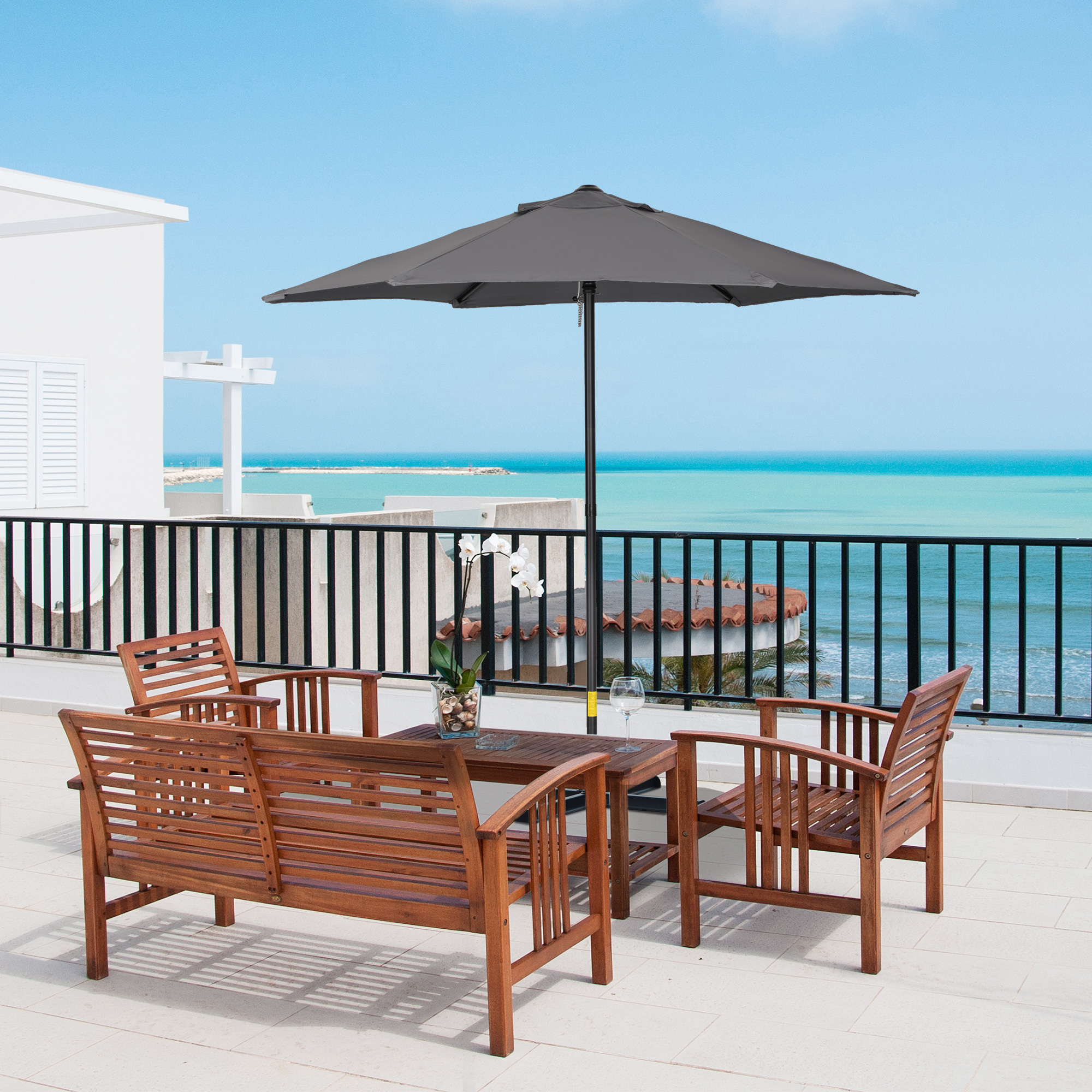 Terrassenszene mit Holzmöbeln, einem grauen Schirm und Meer im Hintergrund.