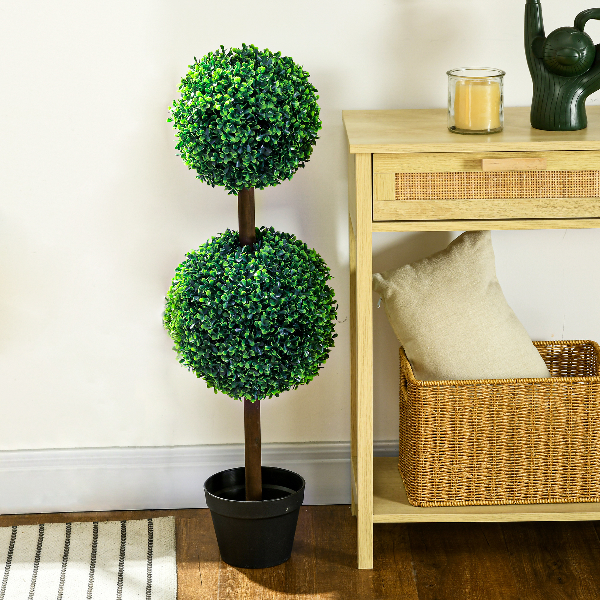Ein Topiari-Baum in einem schwarzen Topf in der Nähe eines Tisches mit Kerze und Korb.