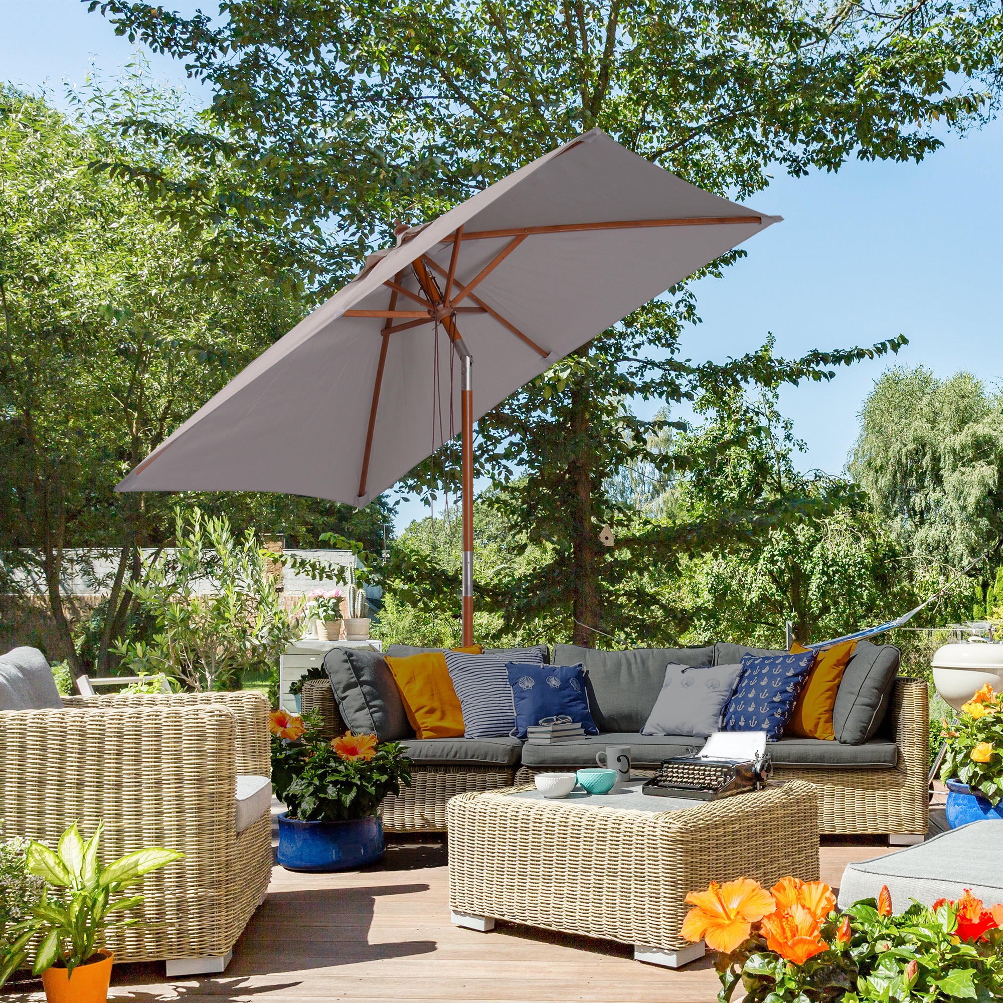 Scena del patio con ombrello grigio aperto, divano, tavolo e piante sotto un cielo blu.