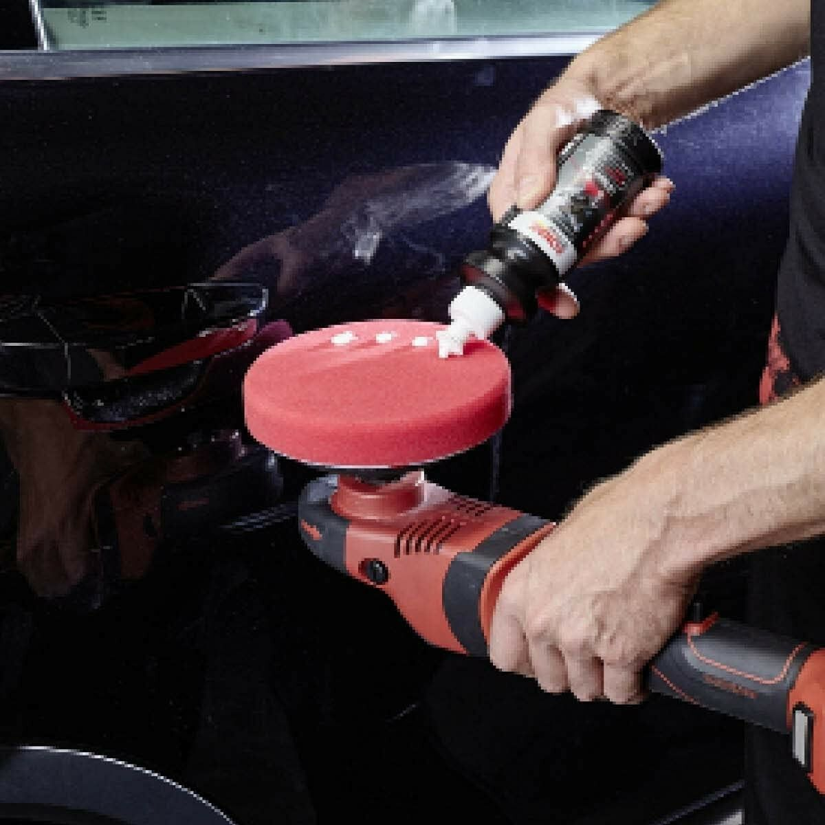 Une personne utilise une polisseuse pour appliquer un composé de polissage sur la surface noire d'une voiture.