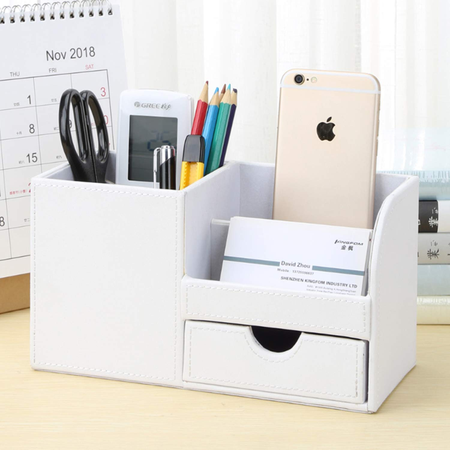 Weißer Schreibtisch-Organizer mit Gegenständen gefüllt, darunter Schere, Stifte, Telefon, Visitenkarten und ein Kalender.