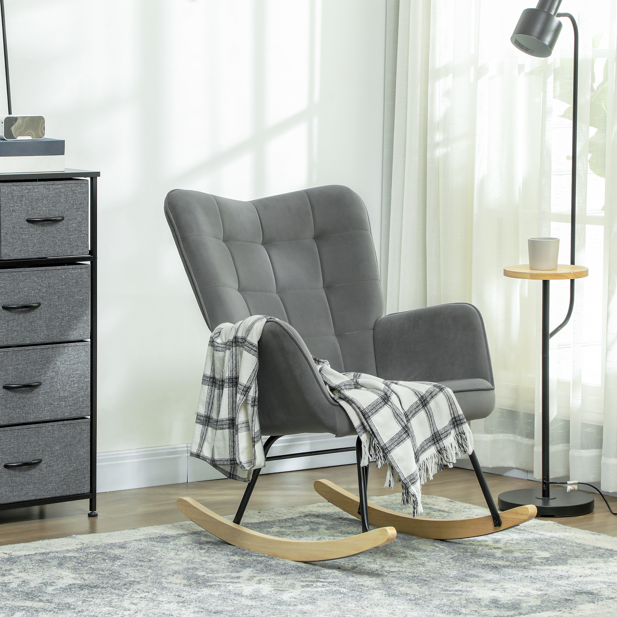 Ein grauer Schaukelstuhl mit Decke, Stehlampe und Kommode.