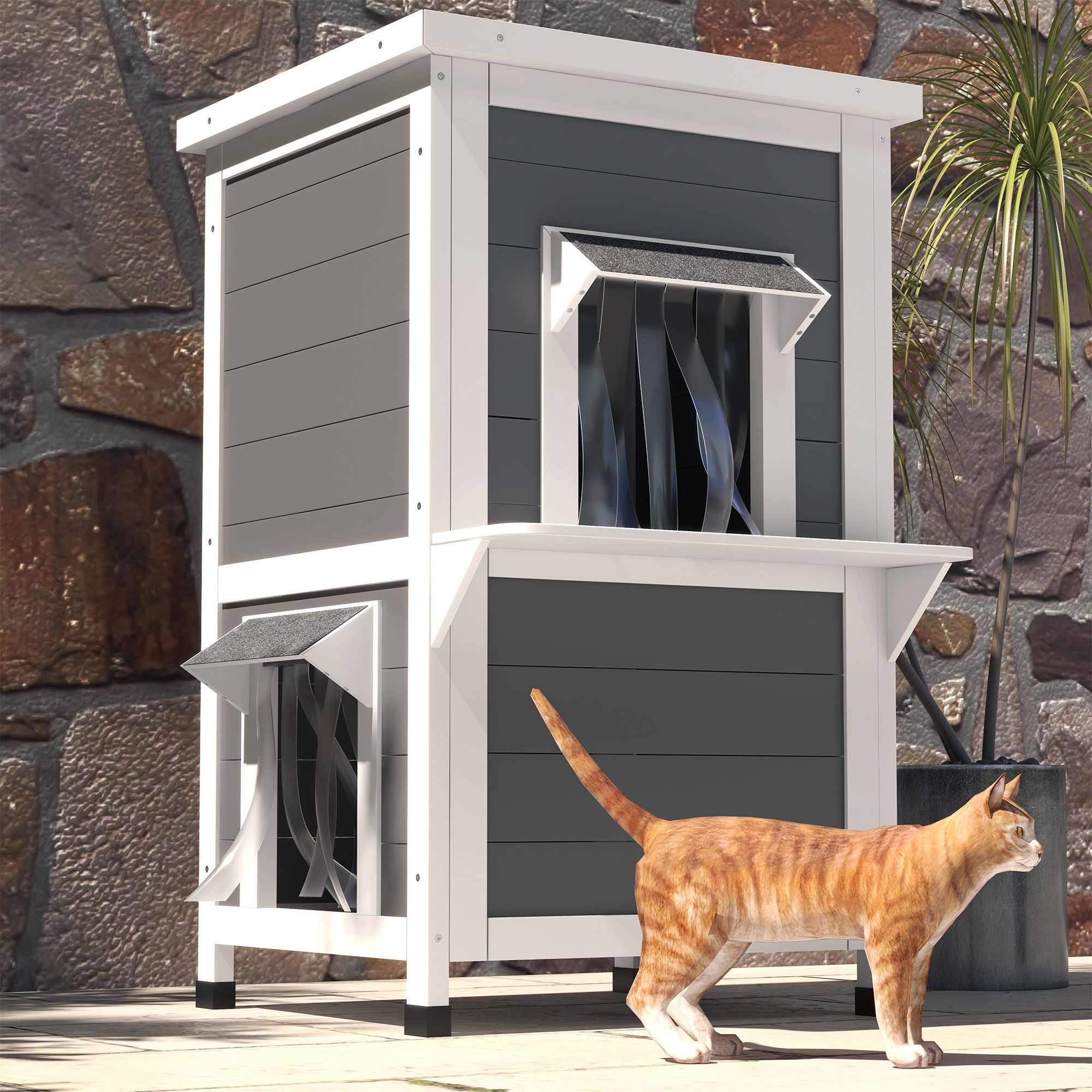 Eine Katze vor einem grau-weißen Katzenhaus. Eine Steinmauer und grüne Pflanzen im Hintergrund.