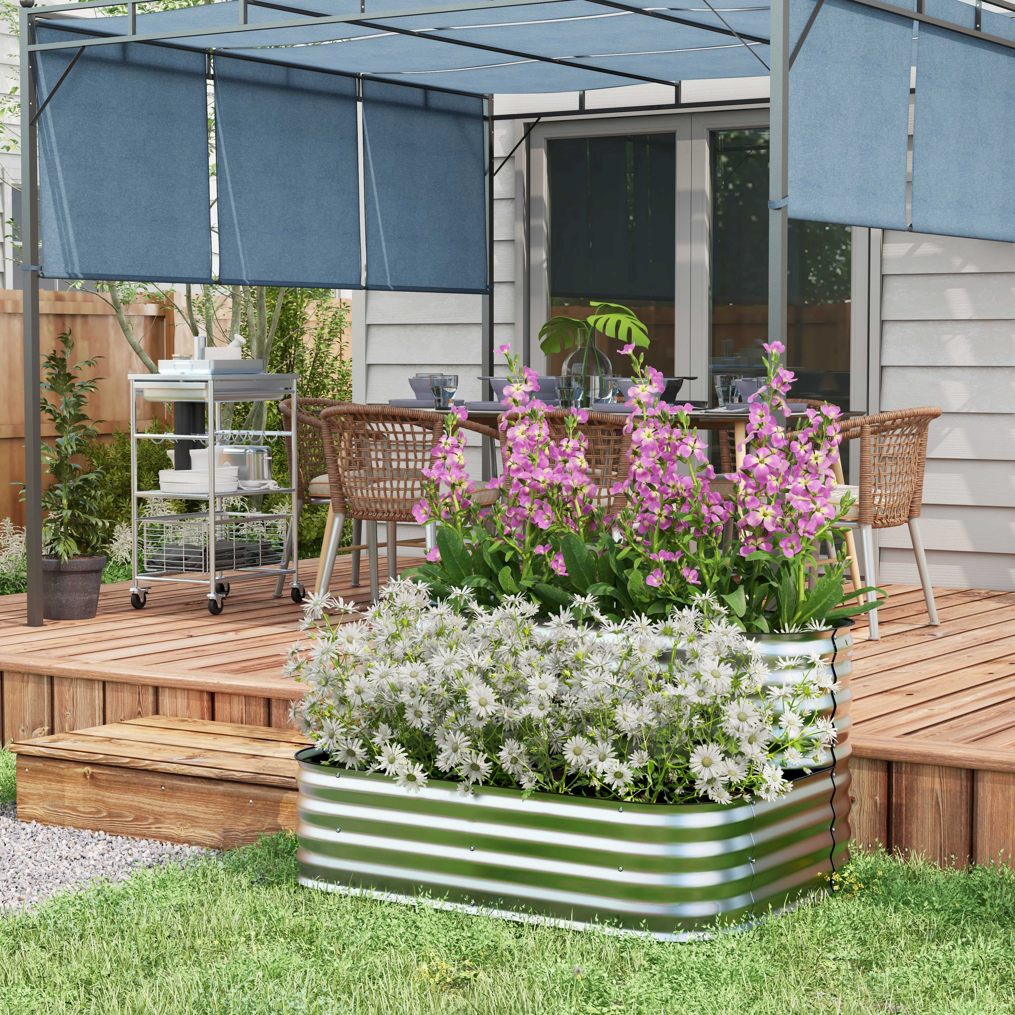 Gartenszene mit einem Metallpflanzkasten. Blumen vor einem Deck und einer Pergola.