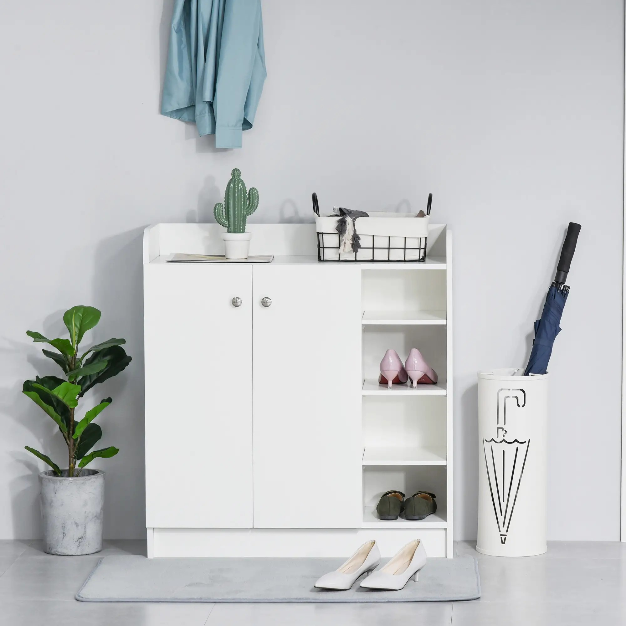 Weißer Schuhschrank mit Pflanze, Kaktus und Schuhen. Ein blauer Mantel hängt darüber. Graue Matte auf dem Boden.