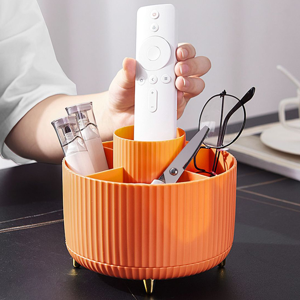 Eine Person hält eine weiße Fernbedienung in einem orangefarbenen Schreibtisch-Organizer mit Brille und Schere.