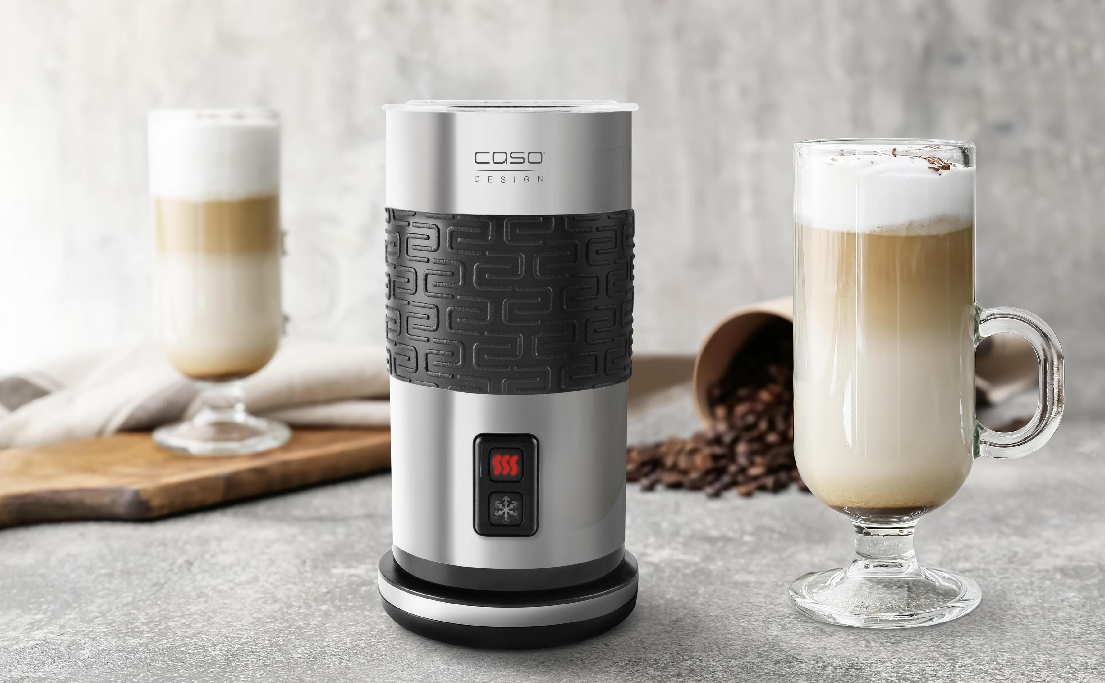 Ein silberner und schwarzer Milchaufschäumer mit zwei Gläsern Latte auf einem Tisch.