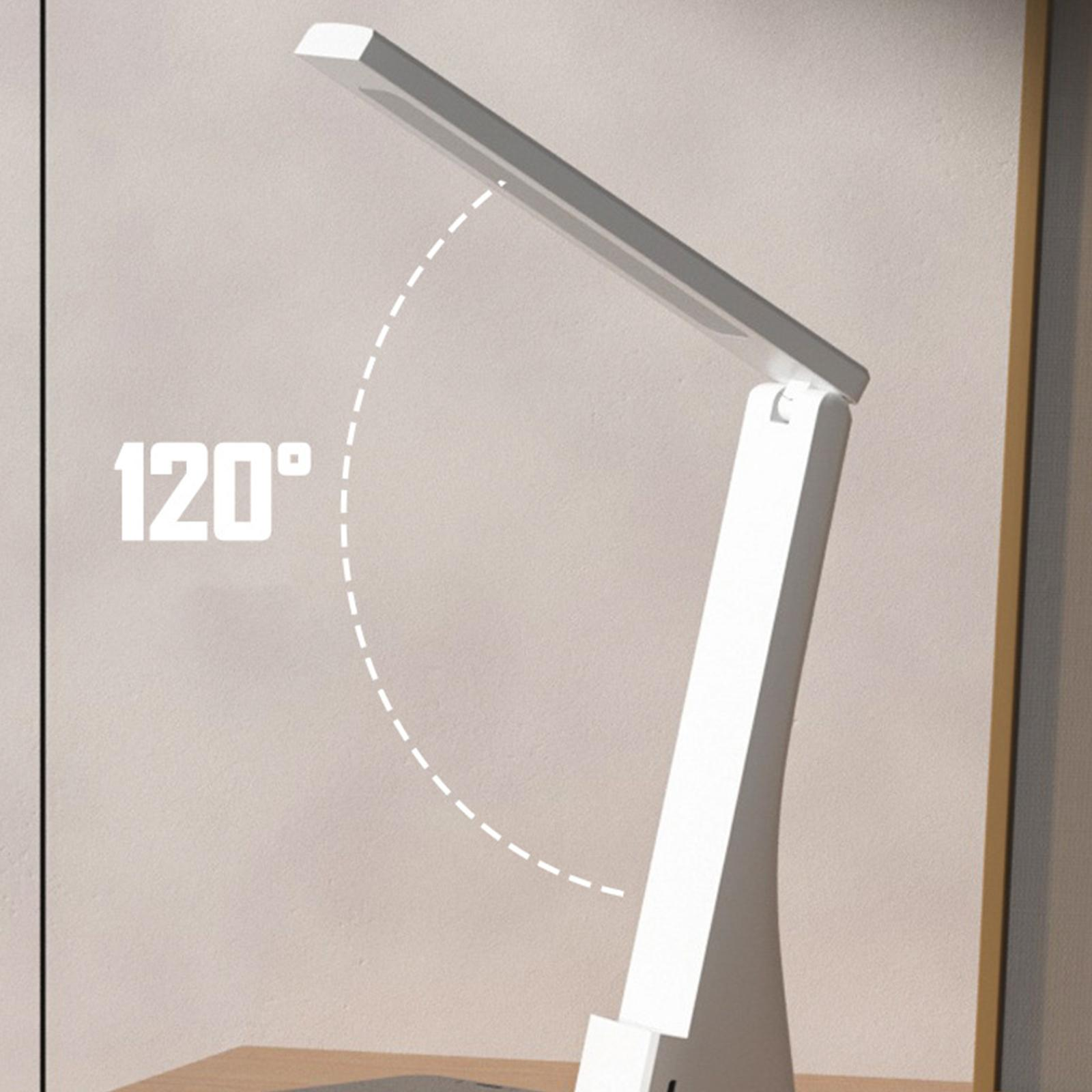 Eine weiße Schreibtischlampe mit einem um 120 Grad geneigten Licht, neben einer Wand, auf einem Holzschreibtisch.