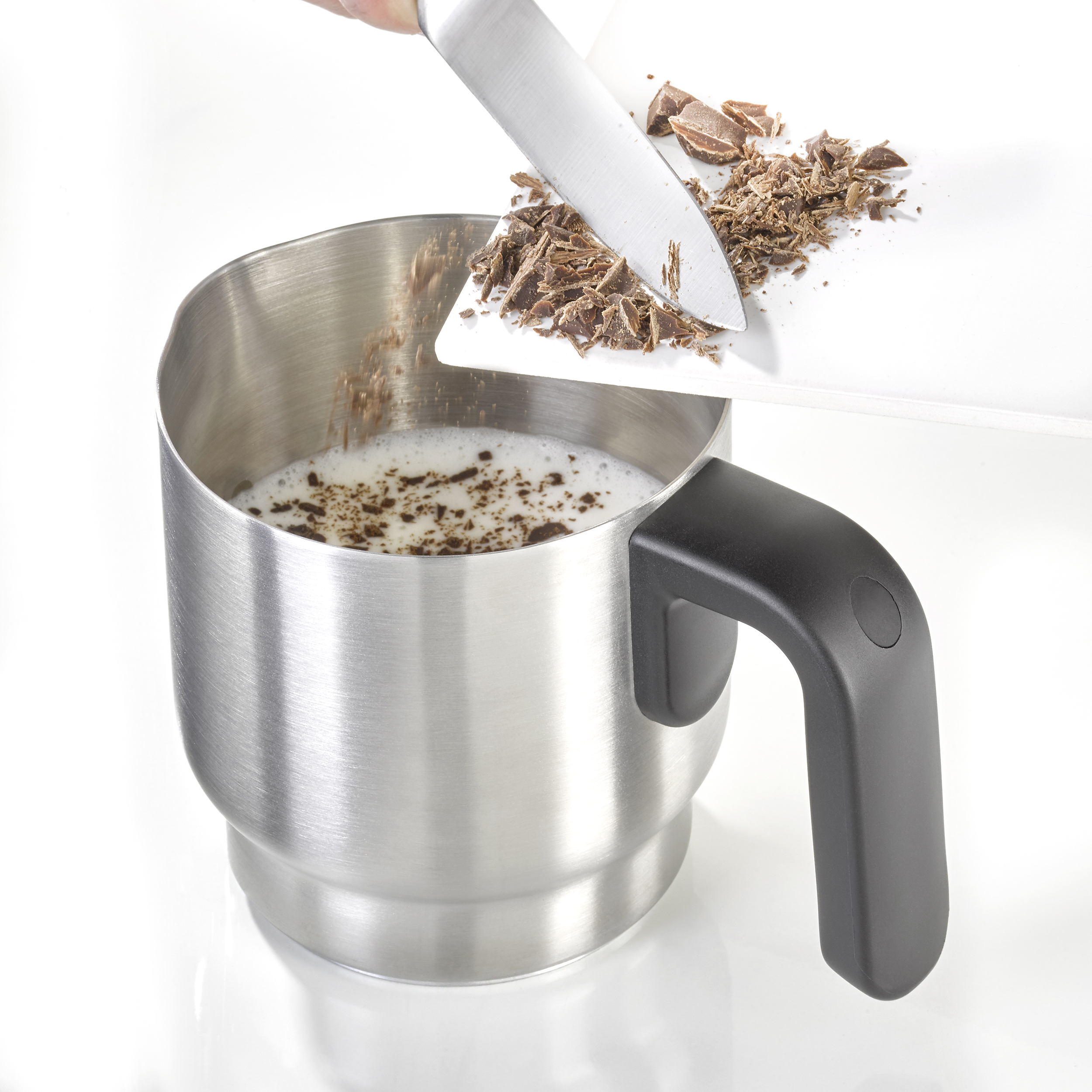 Une main avec un couteau ajoutant des copeaux de chocolat dans une tasse de lait.
