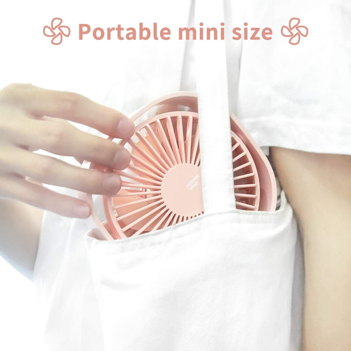 Ein kleiner rosa Ventilator in einer weißen Tasche, die von einer Hand gehalten wird. Der Ventilator hat Flügel und einen kreisförmigen Rahmen.
