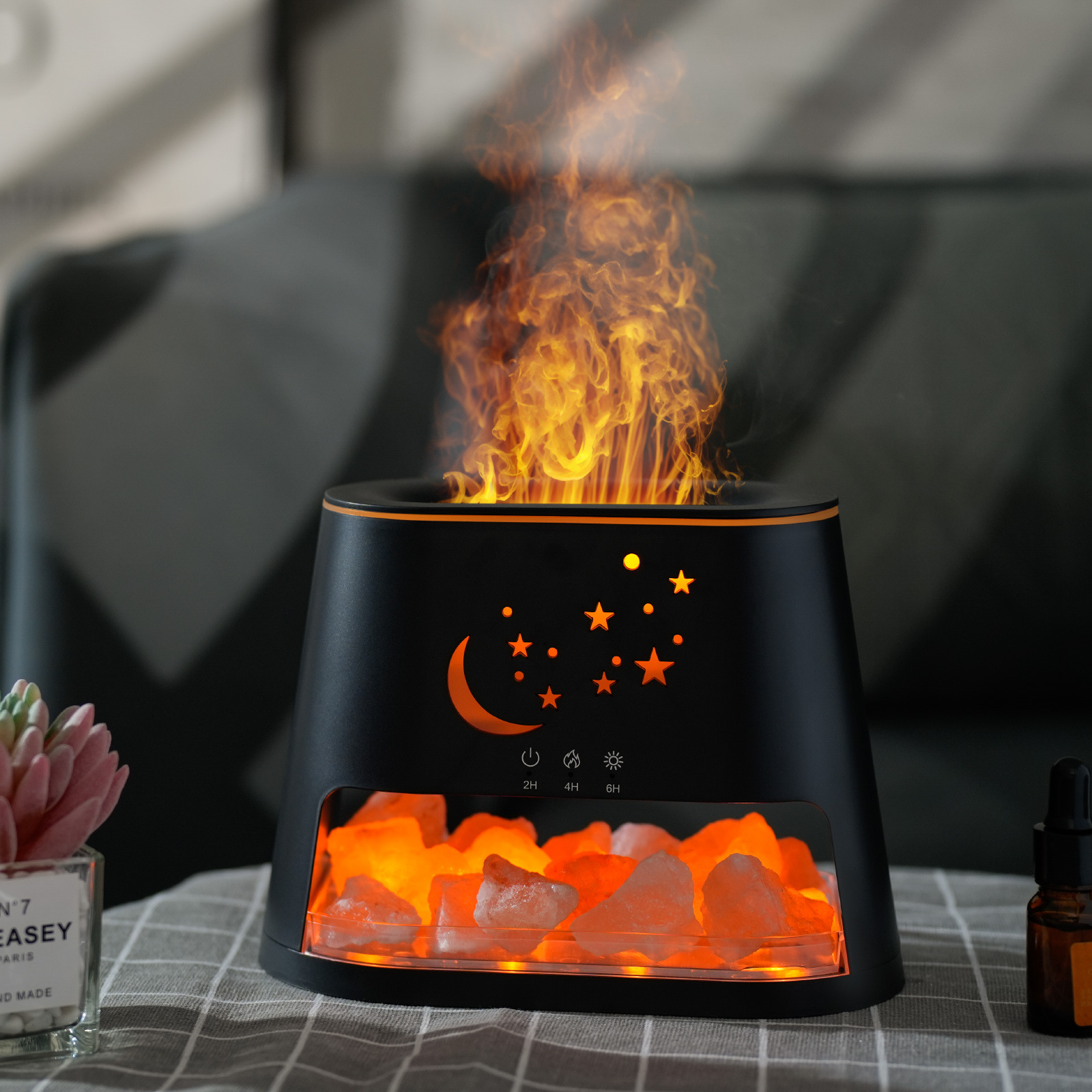 Schwarzer Aromadiffusor mit Flammeneffekt, Sternen und Mond, mit Steinen und Ölflasche auf dem Tisch.