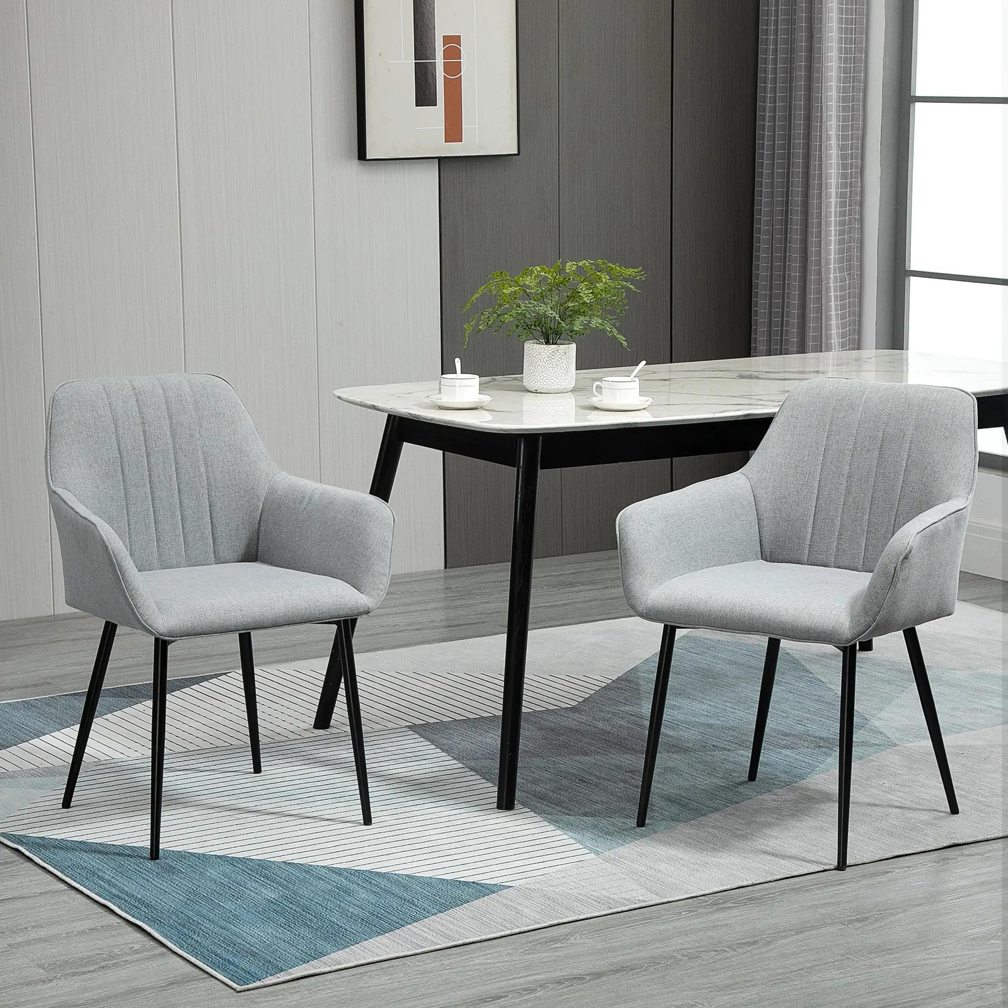 Zwei graue Stühle neben einem Tisch mit einer Pflanze und Tassen. Ein blau-weißer Teppich liegt auf dem Boden.