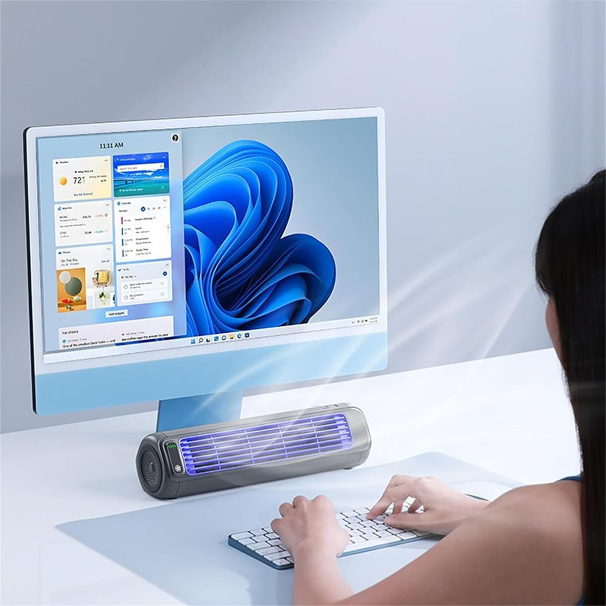 Eine Person benutzt eine Tastatur vor einem Computer, der einen Bildschirm mit mehreren Fenstern und einen Ventilator auf dem Schreibtisch anzeigt.