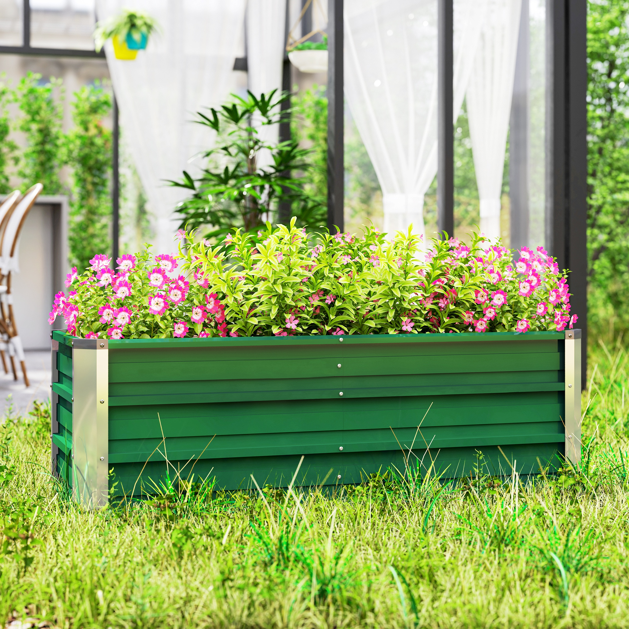 Eine grüne Pflanzkasten mit rosa Blumen gefüllt. Hintergrund zeigt ein Haus und Grün. Gras vorne.