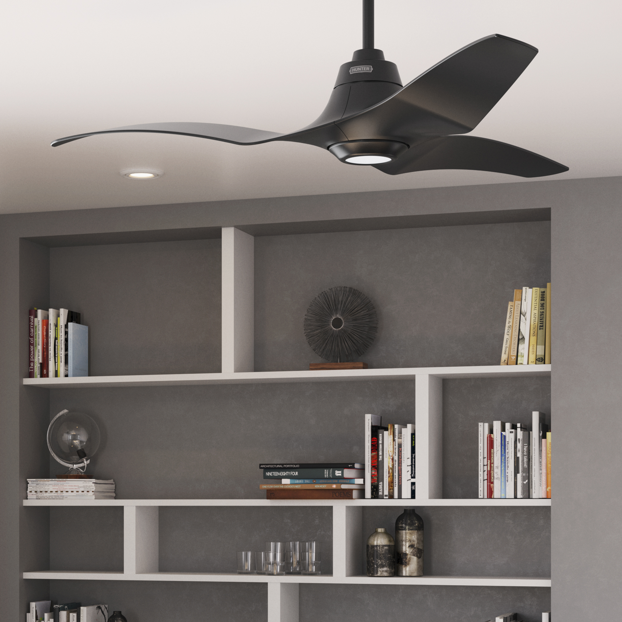Ein schwarzer Deckenventilator mit drei Flügeln ist in einem Raum mit Bücherregalen und einer grauen Wand installiert.