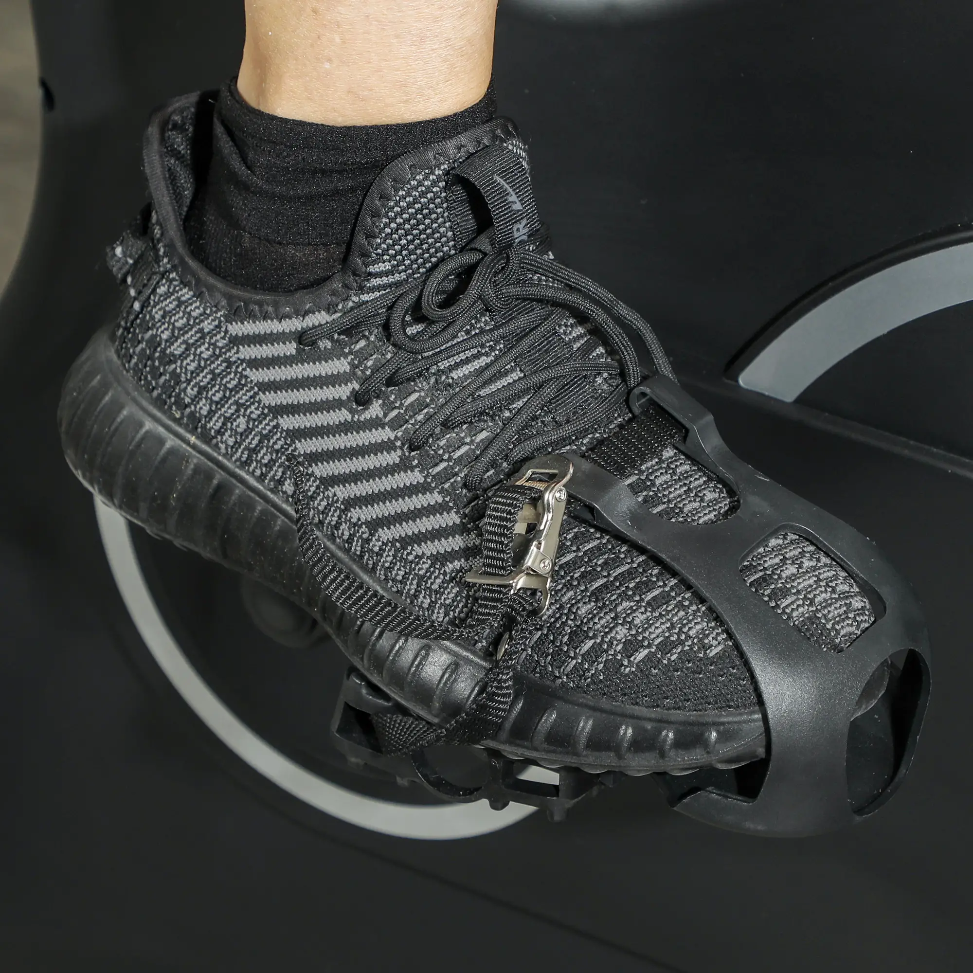 Der Fuß einer Person in einem schwarz-grauen Turnschuh, der an einem schwarzen Fitnessbike-Pedal befestigt ist.