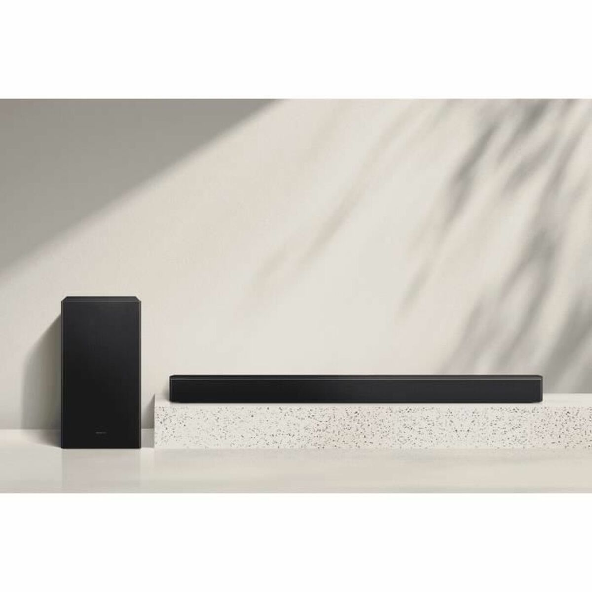 Eine schwarze Soundbar und ein Subwoofer auf einer weißen Oberfläche vor einer weißen Wand. Die Soundbar ist schlank.