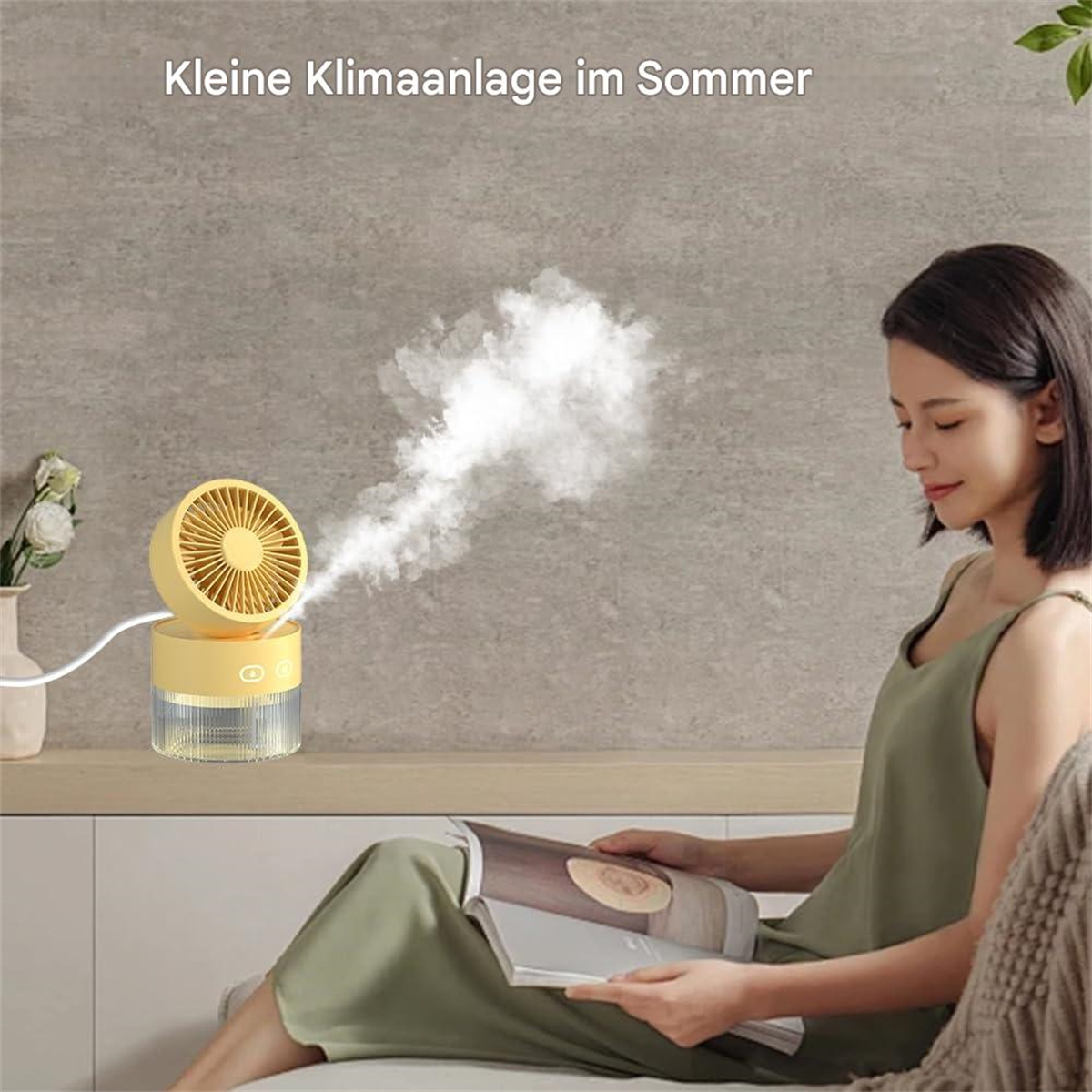 Eine Frau sitzt mit einem Buch in der Nähe eines kleinen gelben Ventilators. Der Ventilator stößt Nebel aus. Die Szene ist drinnen.