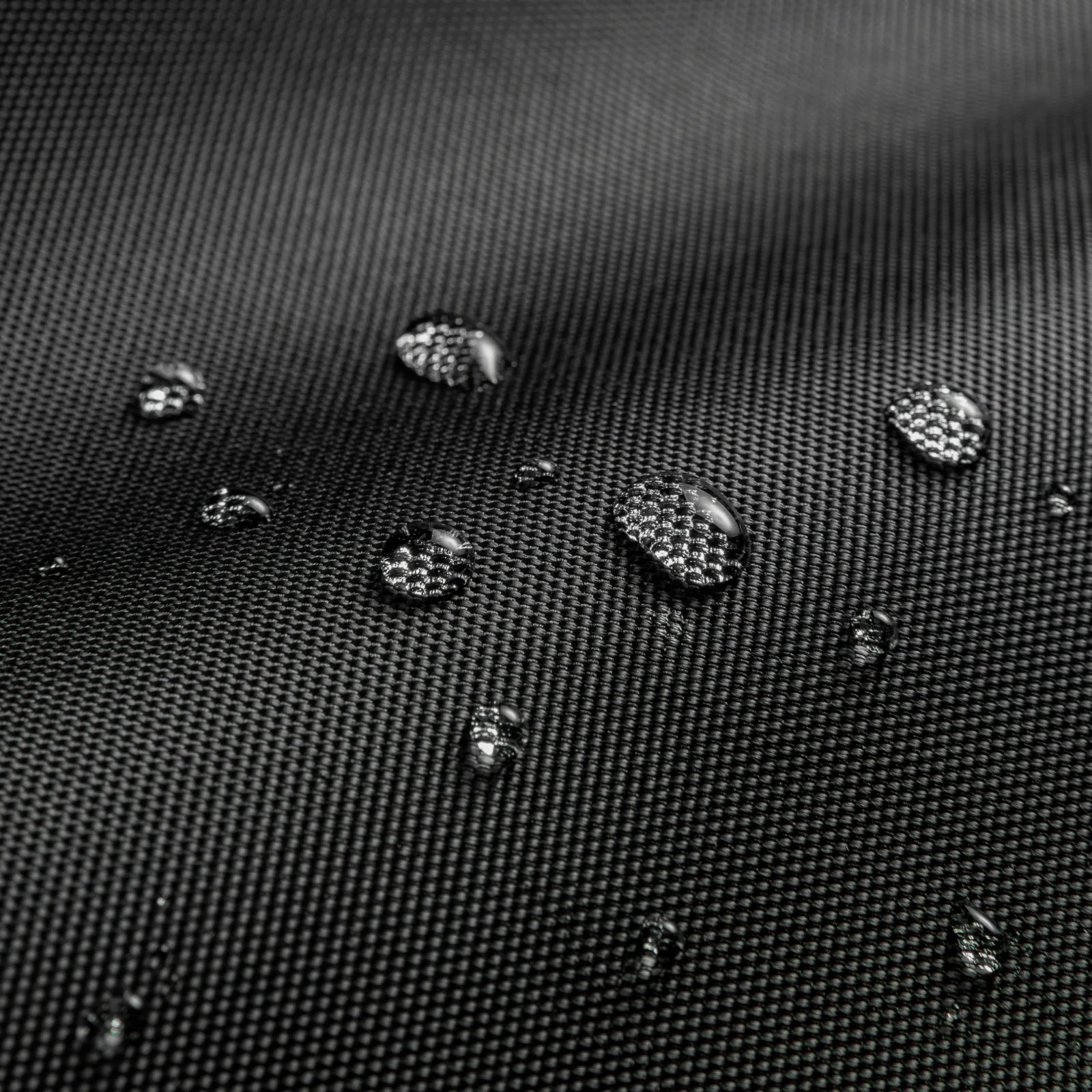 Zbliżenie czarnej tkaniny z kroplami wody. Krople są przezroczyste, odbijają światło. Tkanina ma teksturowany splot.