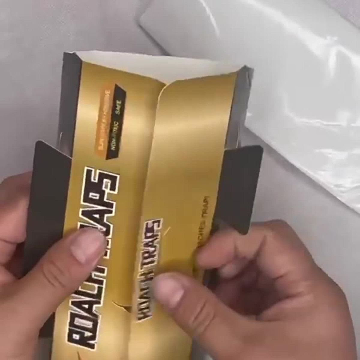 Hände öffnen eine Schachtel mit Roach Traps. Die Schachtel hat goldfarbene Schrift und ist ungiftig und sicher.