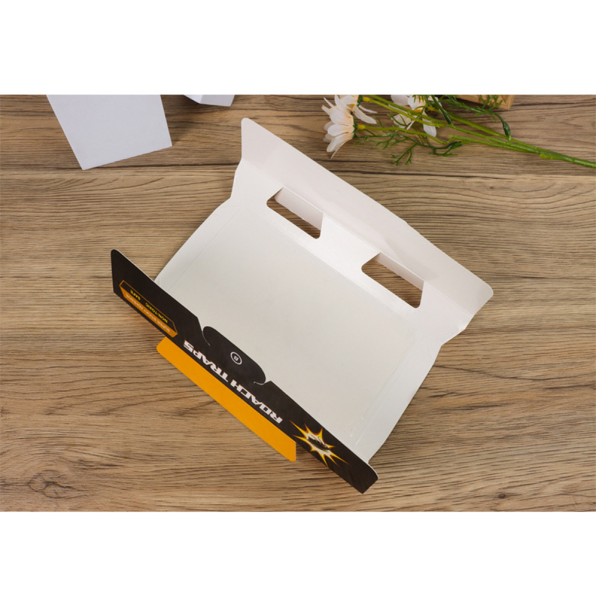 Kakerlakenfallen-Verpackung offen auf einem Holztisch. Die Falle ist schwarz und gold, weiße Verpackung dahinter. Details der Falle.