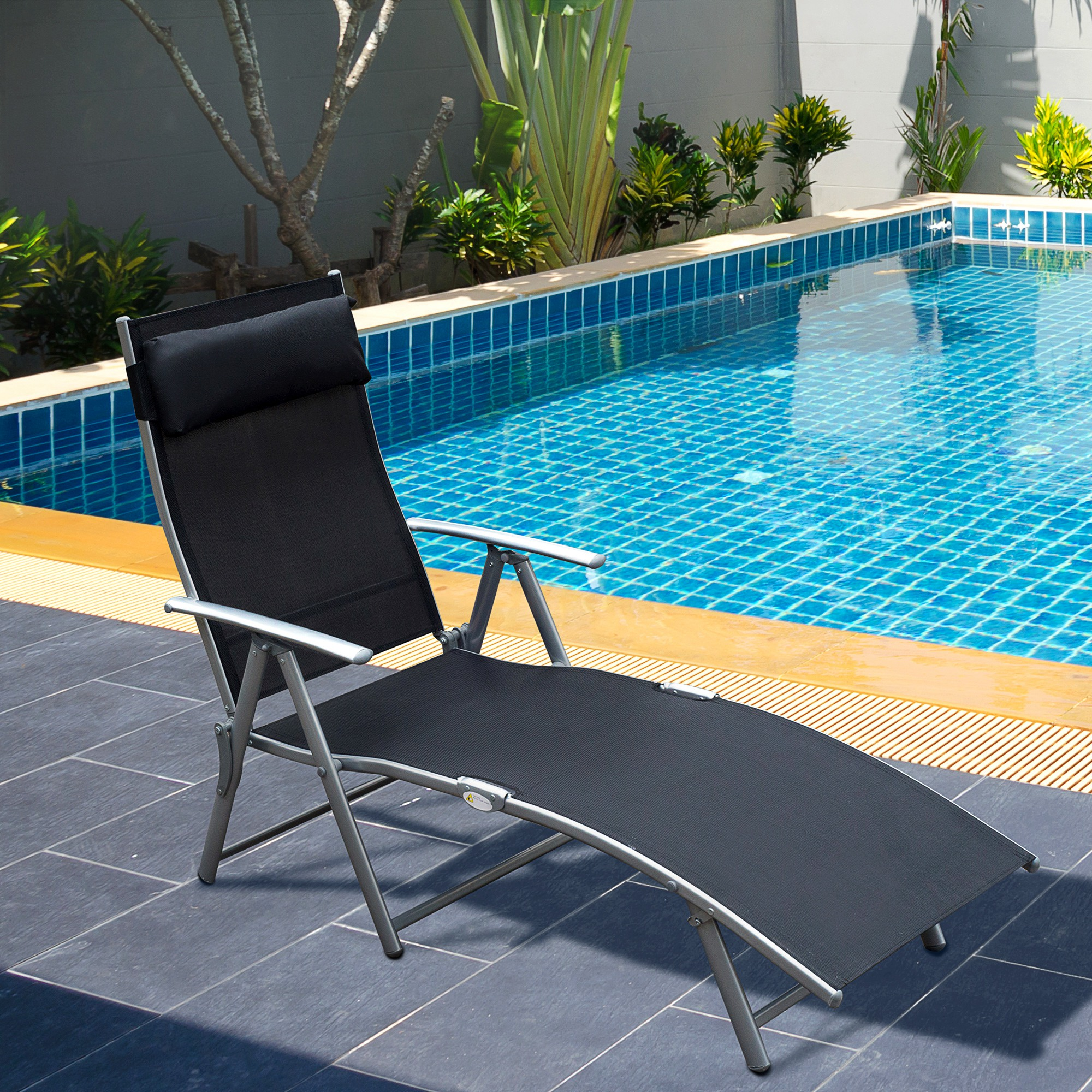 Una sedia reclinabile nera vicino a una piscina. La piscina ha piastrelle blu e cielo sereno.