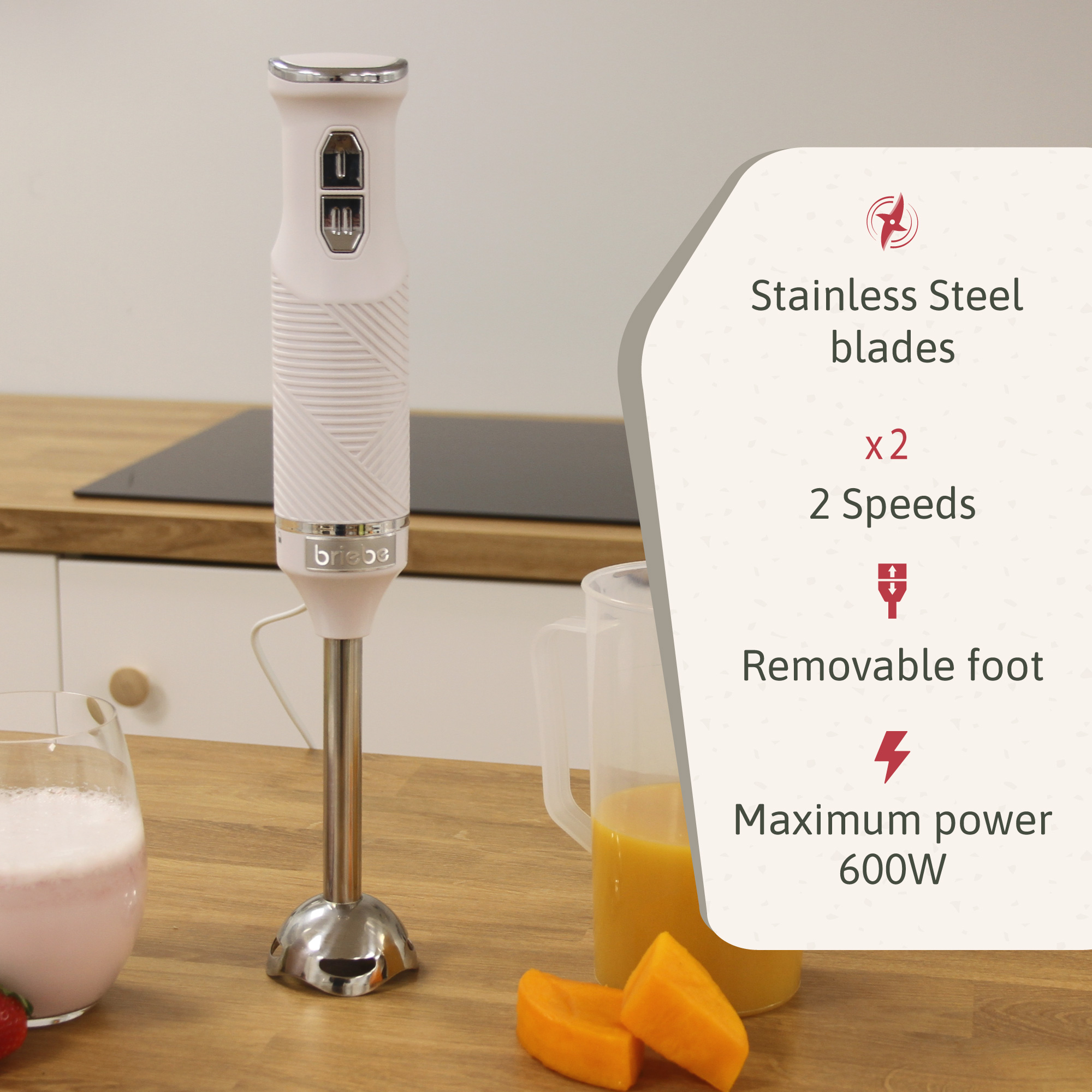 Una batidora de inmersión Briebe Home blanca sobre una superficie de madera, con rodajas de naranja y un vaso de bebida rosa.
