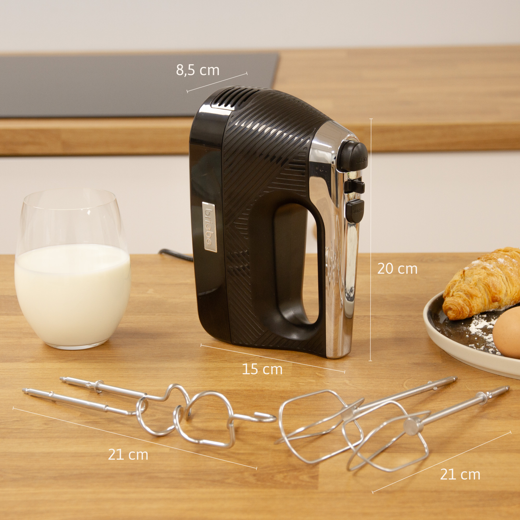 Batidora eléctrica negra con dimensiones mostradas, junto a un vaso de leche e ingredientes para hornear.