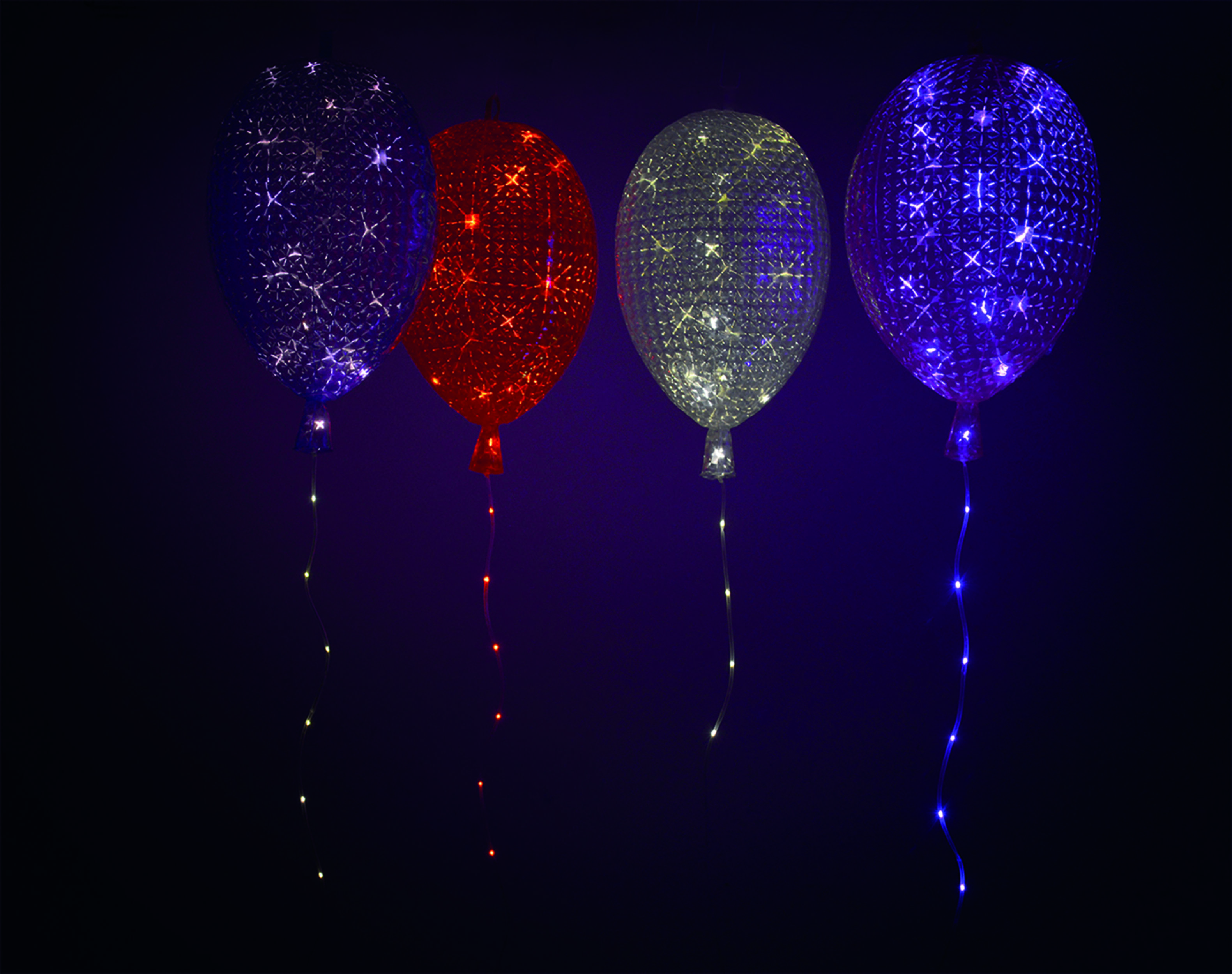 Vier beleuchtete Ballons, jeweils in verschiedenen Farben. Sie befinden sich in einer dunklen Umgebung und strahlen sanft.