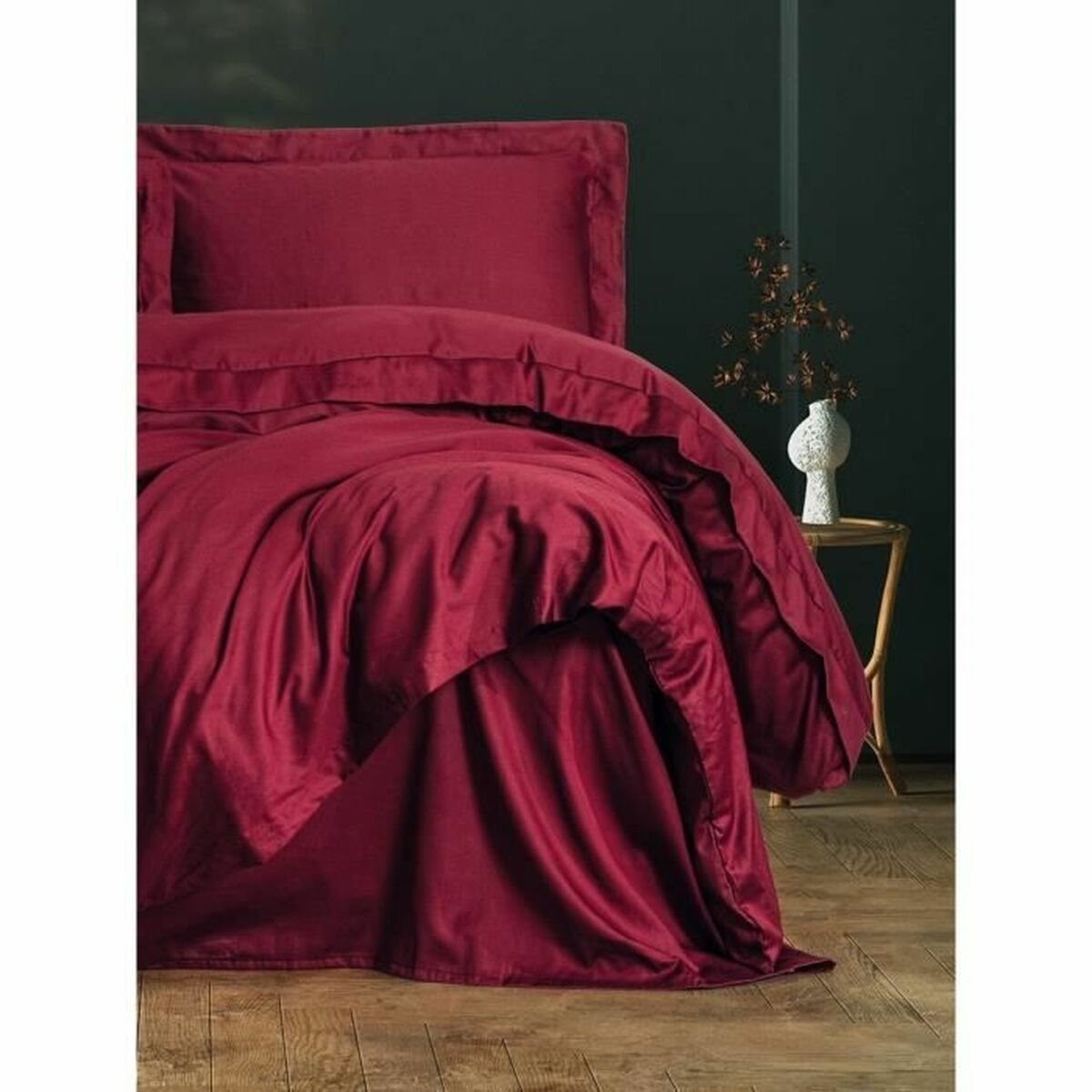 Ein Bett mit roter Bettdecke und Kissen. Der Raum hat dunkelgrüne Wände und eine weiße Vase.