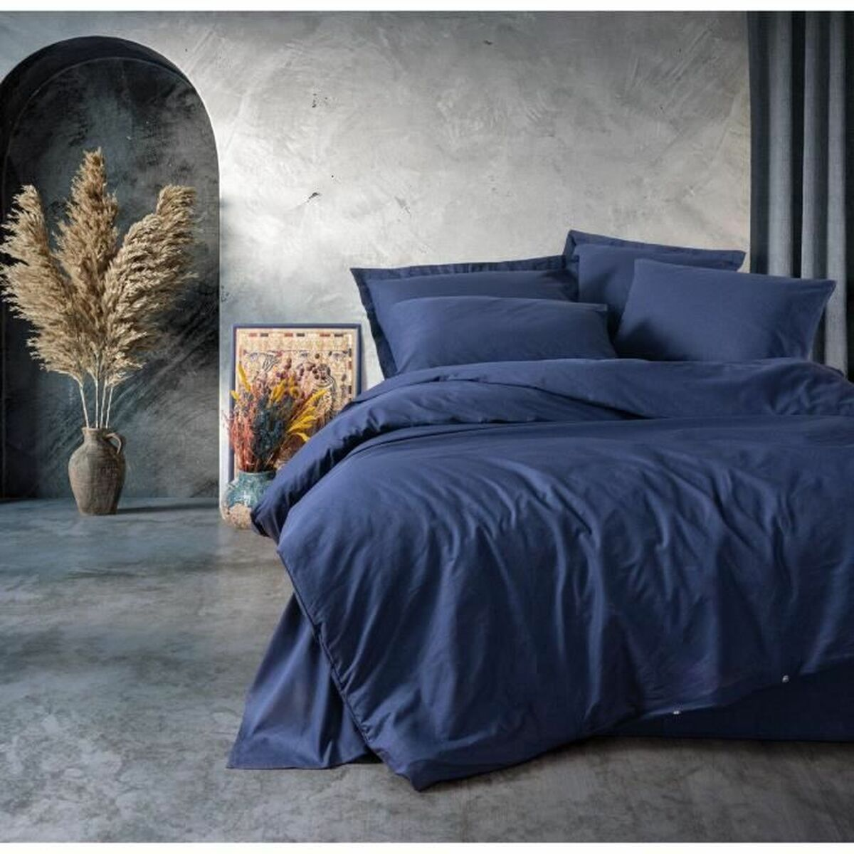 Blaue Bettwäsche auf einem Bett, mit Vase und Bilderrahmen.