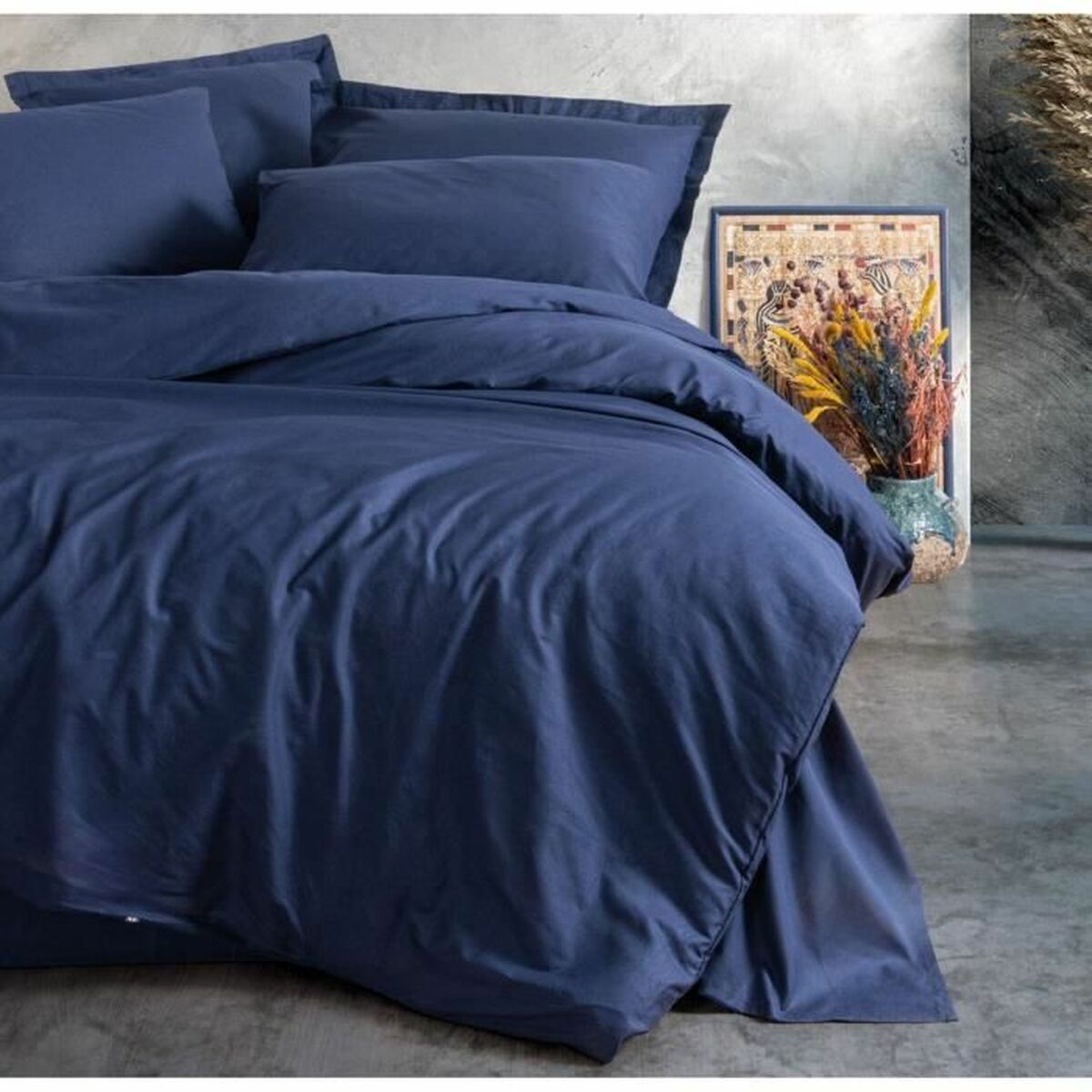 Blaue Bettwäsche auf dem Bett, mit Vase und Gemälde im Hintergrund.