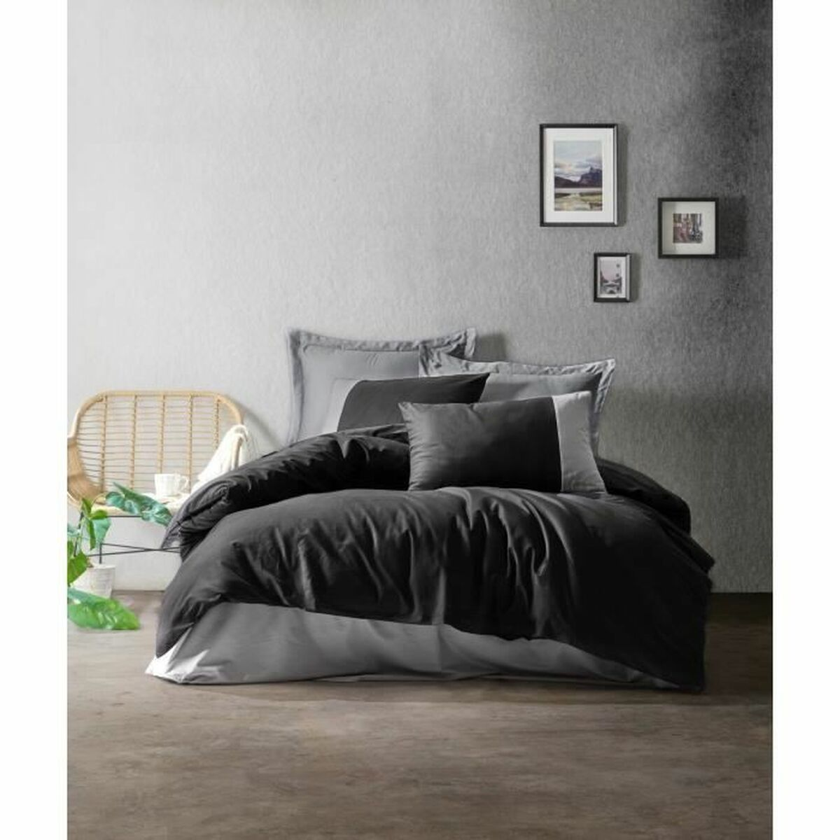 Schlafzimmer mit schwarzer Bettwäsche, zwei Kissen. Graue Wände, Kunstwerke und ein Stuhl sind zu sehen.
