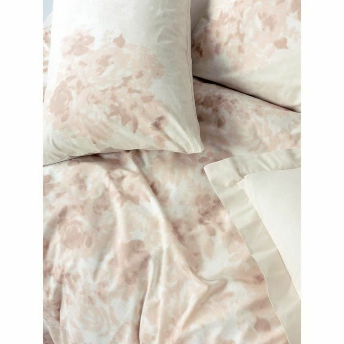 Nahaufnahme eines Bettes mit floral gemusterter Bettwäsche. Kissen und eine Decke sind sichtbar.