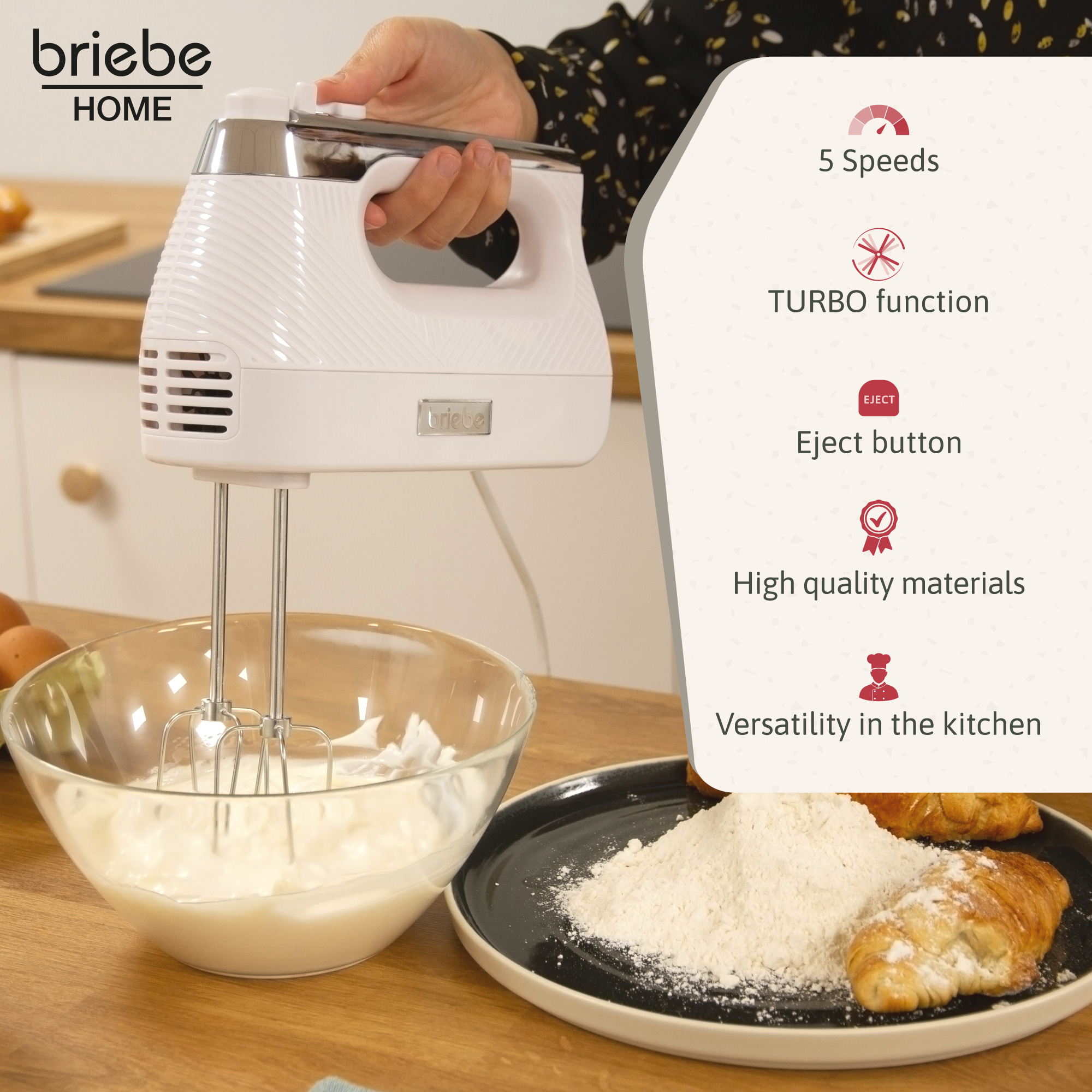 Una batidora de mano blanca batiendo crema. En la mesa hay un plato con harina y un cruasán.